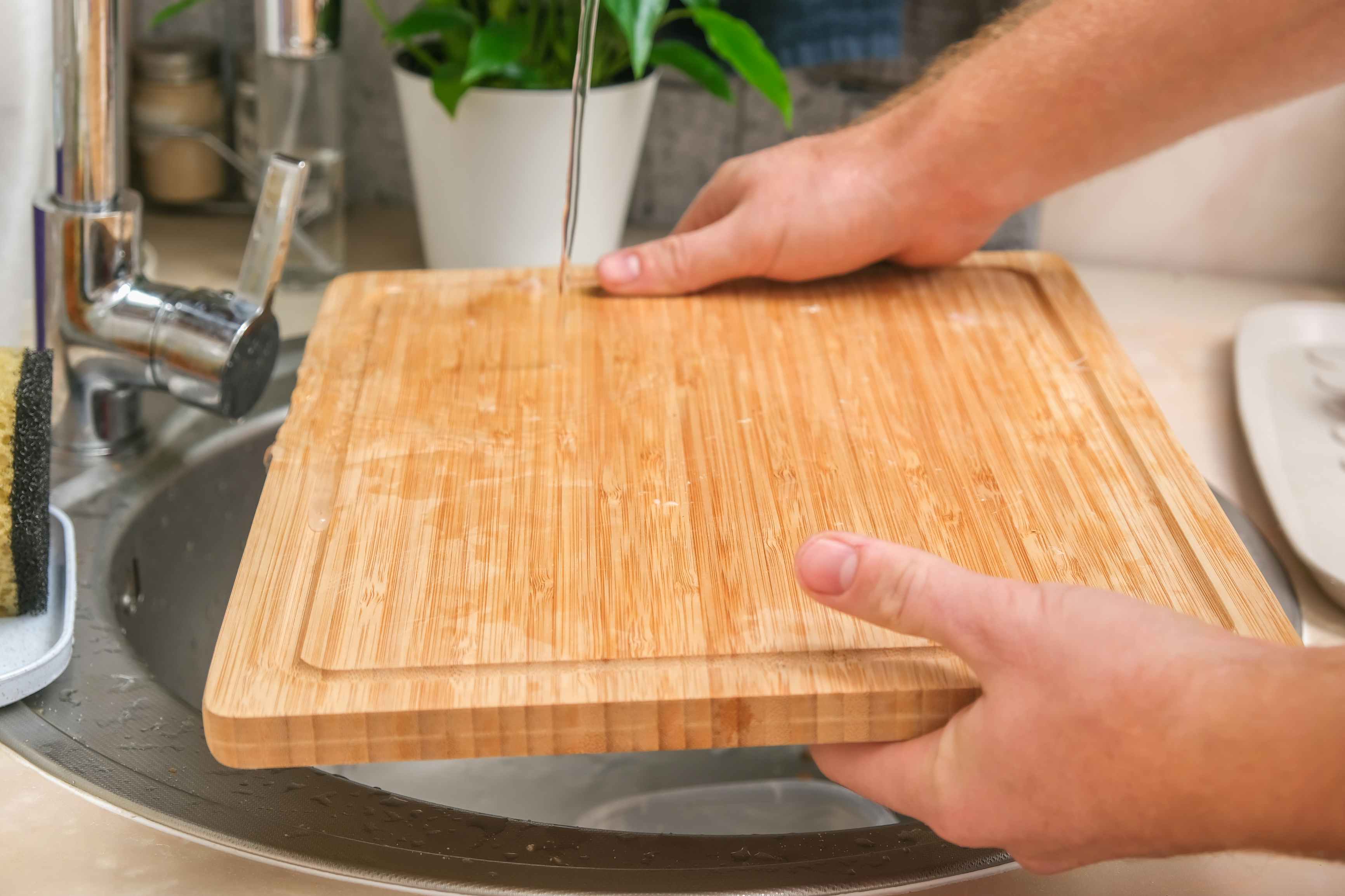 Someone rinsing a wood cutting board in a sink