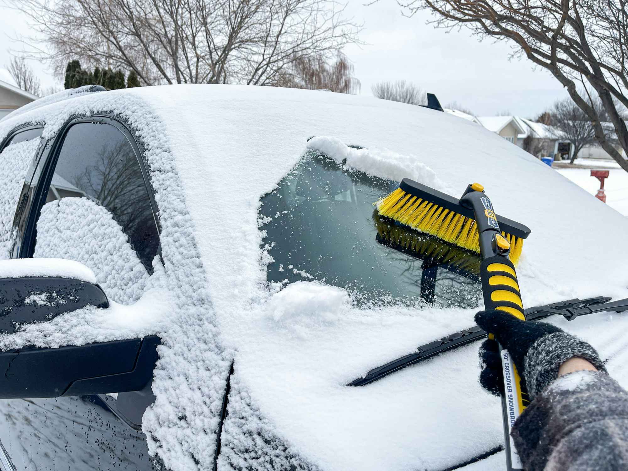 Someone brushing snow off of their vehicle's windshield that is not frosted over