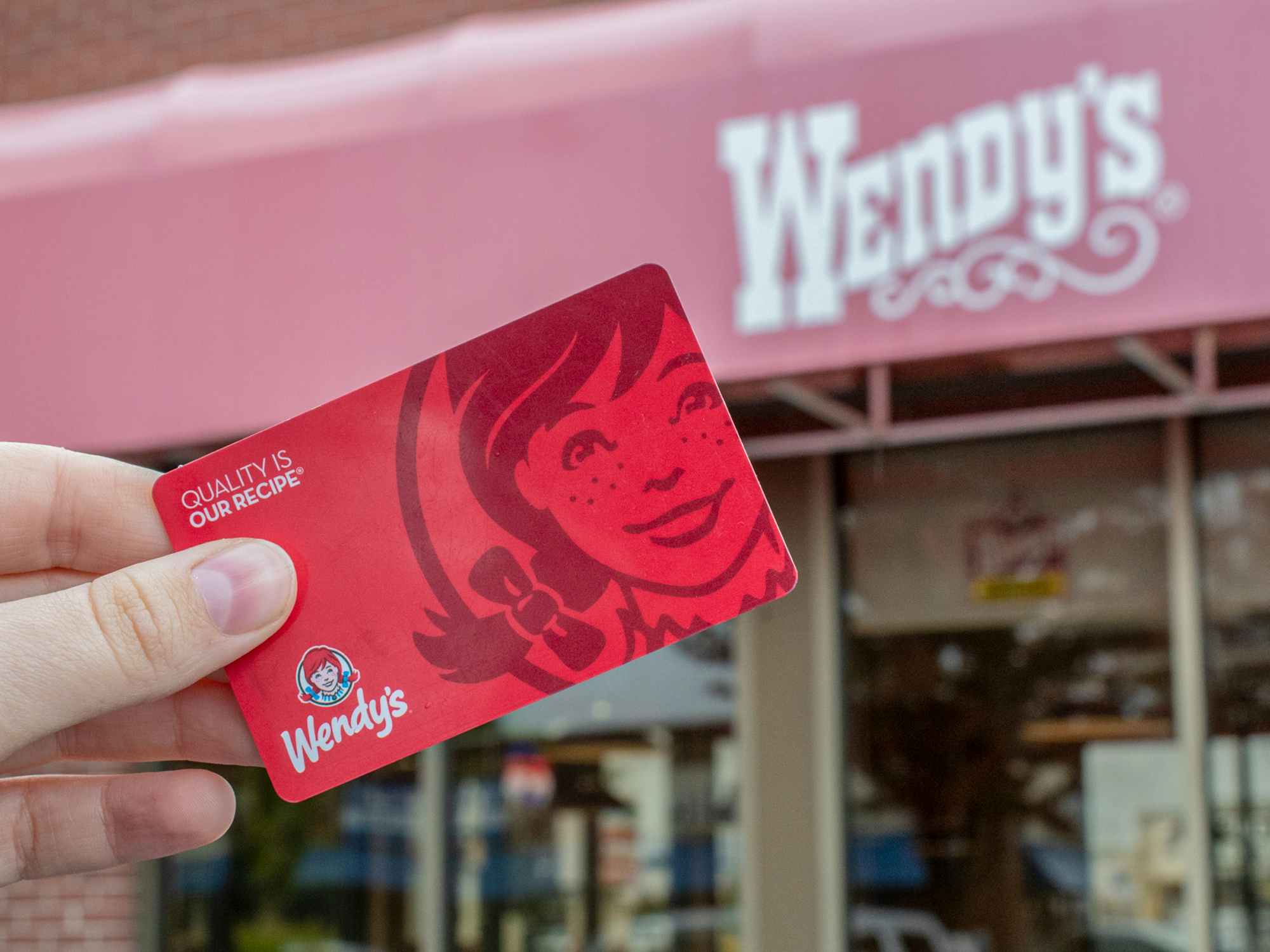 a person holding a wendys gift card outside of a wendys restaurant 
