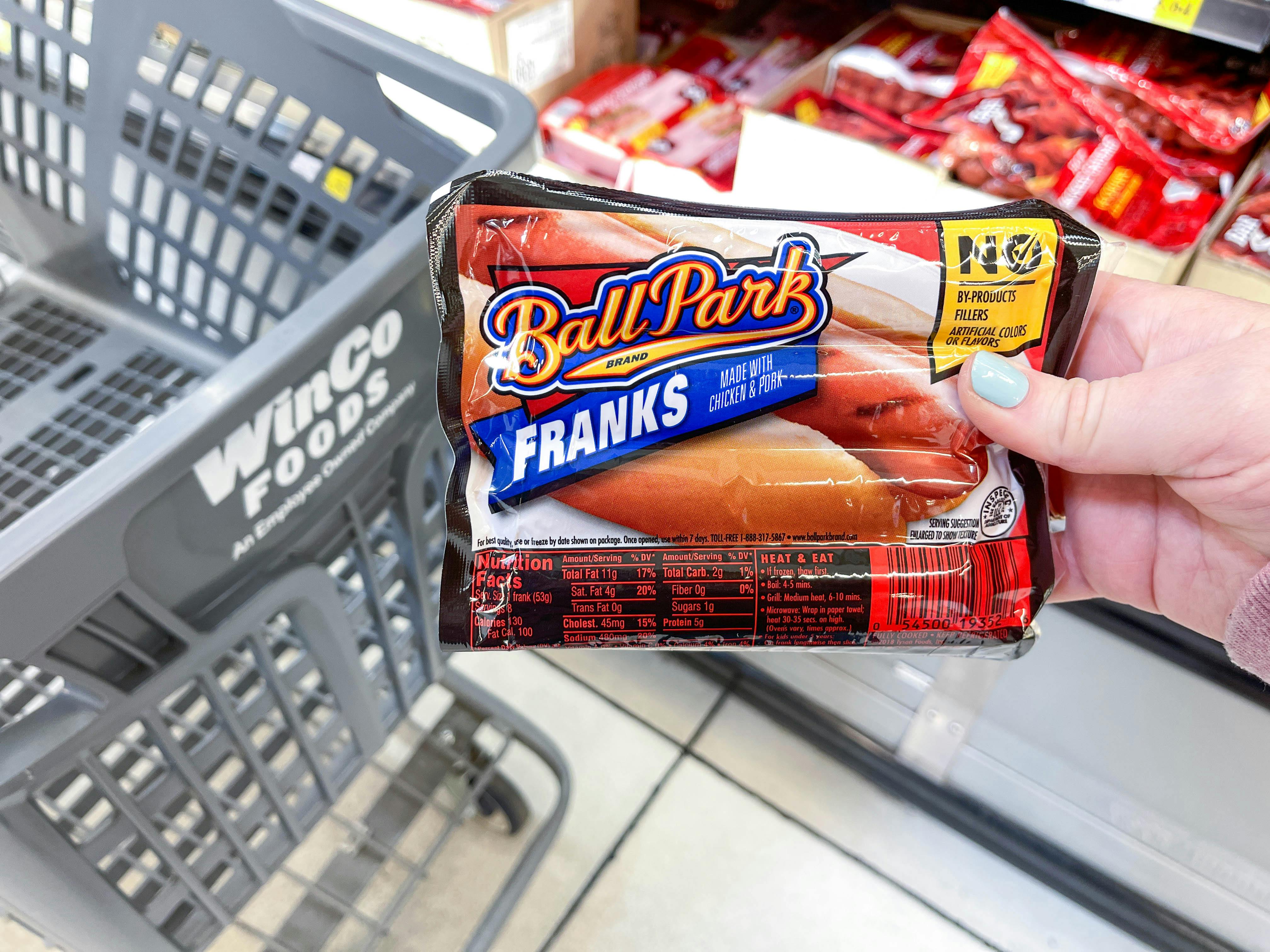 a person holding up ballpark hot dogs in front of cart