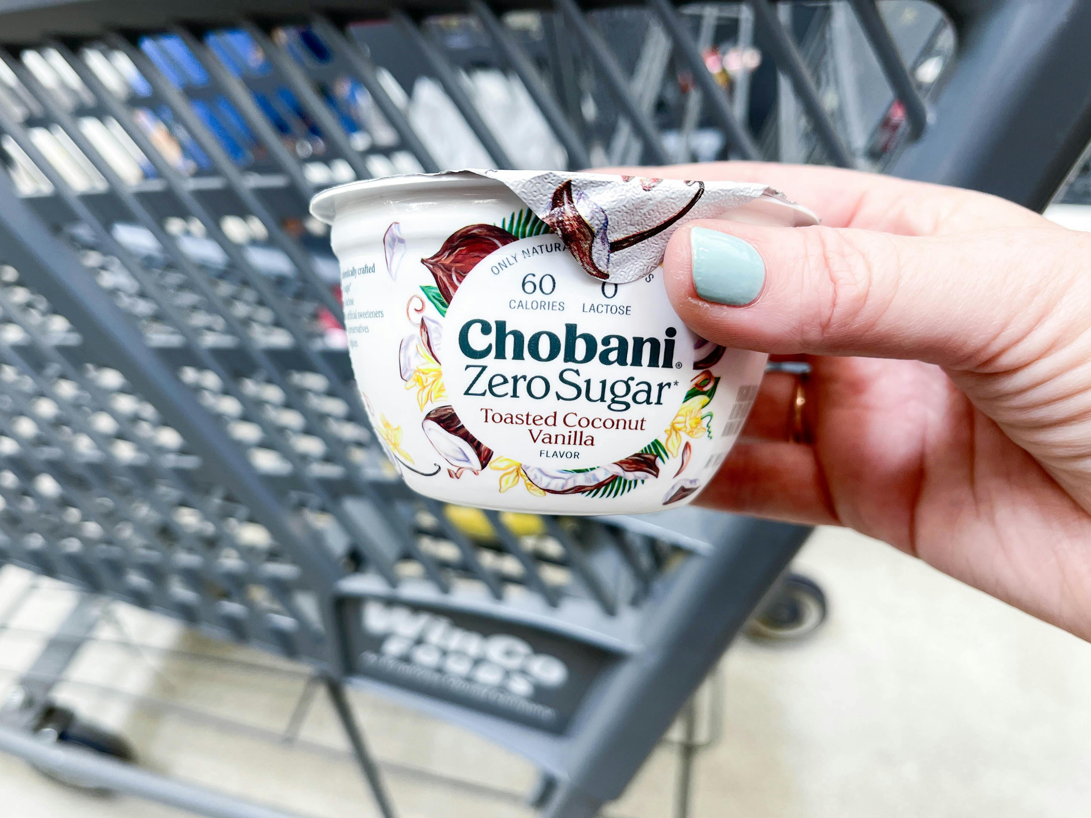 a person holding up chobani yogurt in front of cart