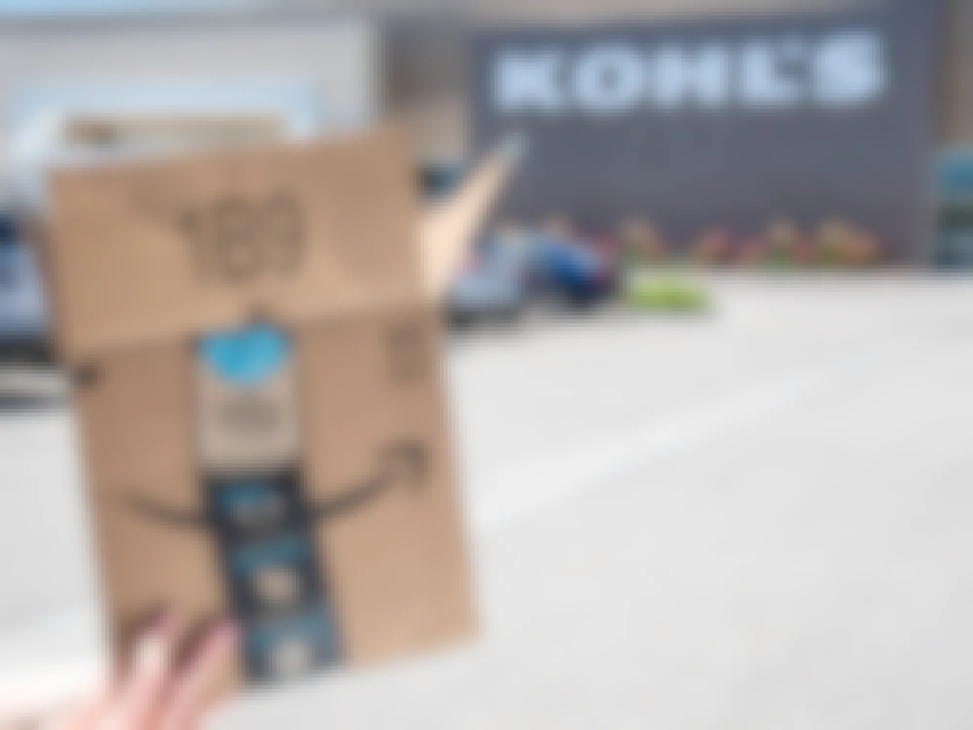 A person holding an open Amazon box in front of Kohl's
