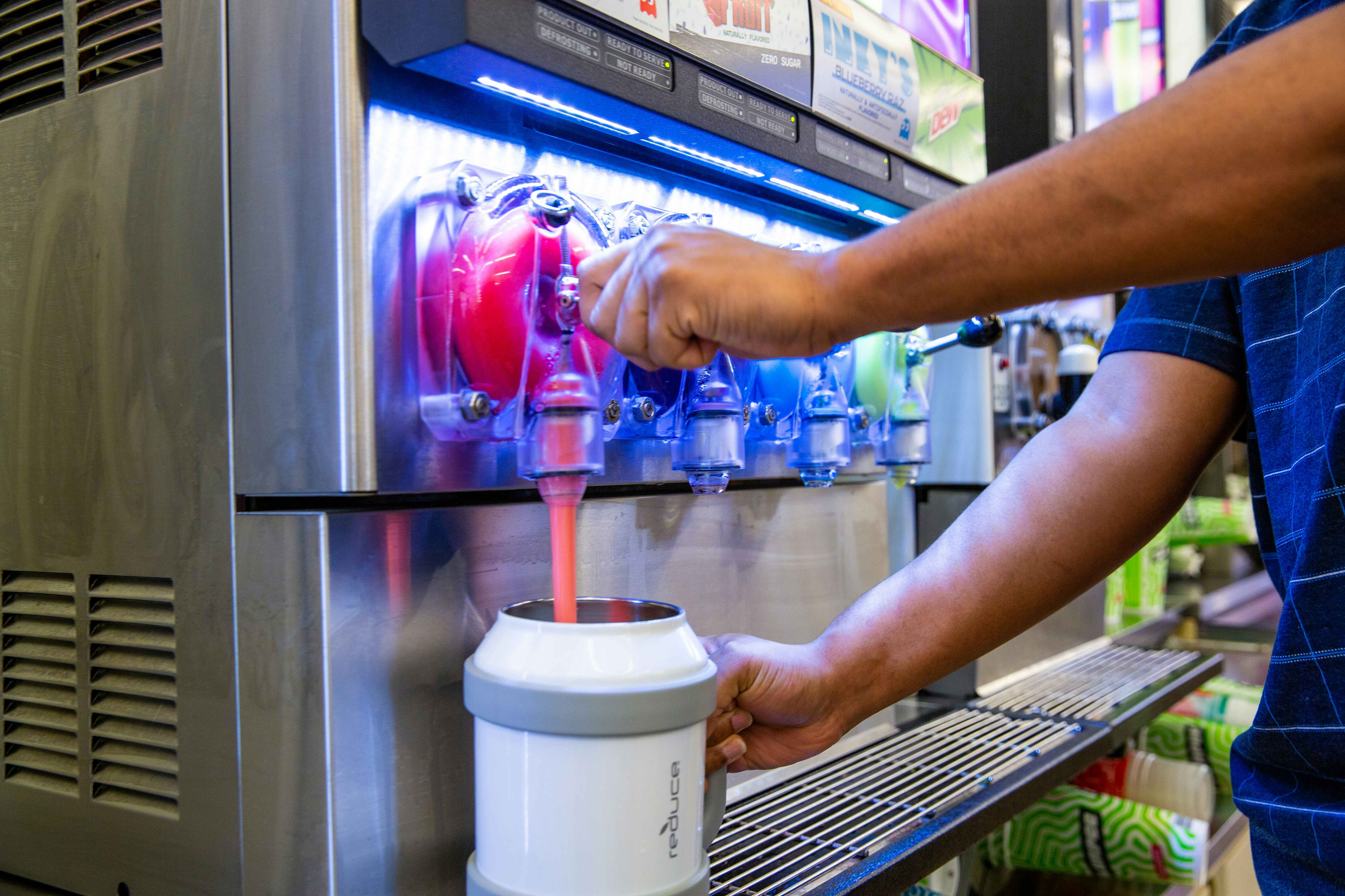 Someone using the slurpee machine in a very large insulated cup
