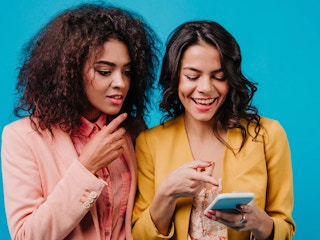 Two women standing while looking at a phone.