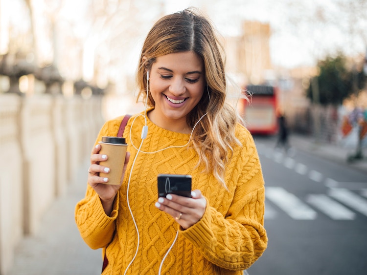 happy person outside in the city with coffee, phone, and headphones
