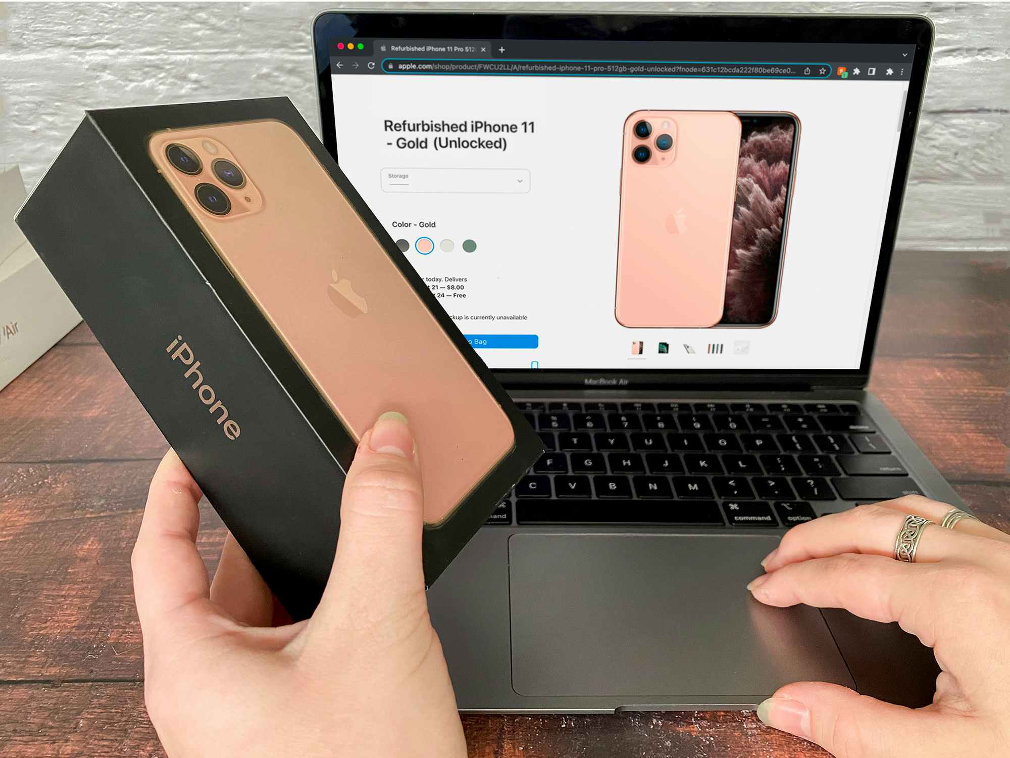 Someone holding an iPhone box next to a laptop displaying the same phone on the Apple Refurbished webpage
