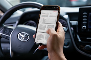 Someone looking at the declaration page of their car insurance policy on their phone while sitting in a car