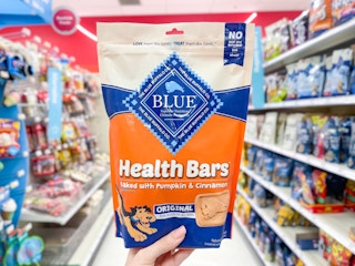 A package of Blue Buffalo Health Bars held out by hand in front of a store aisle.
