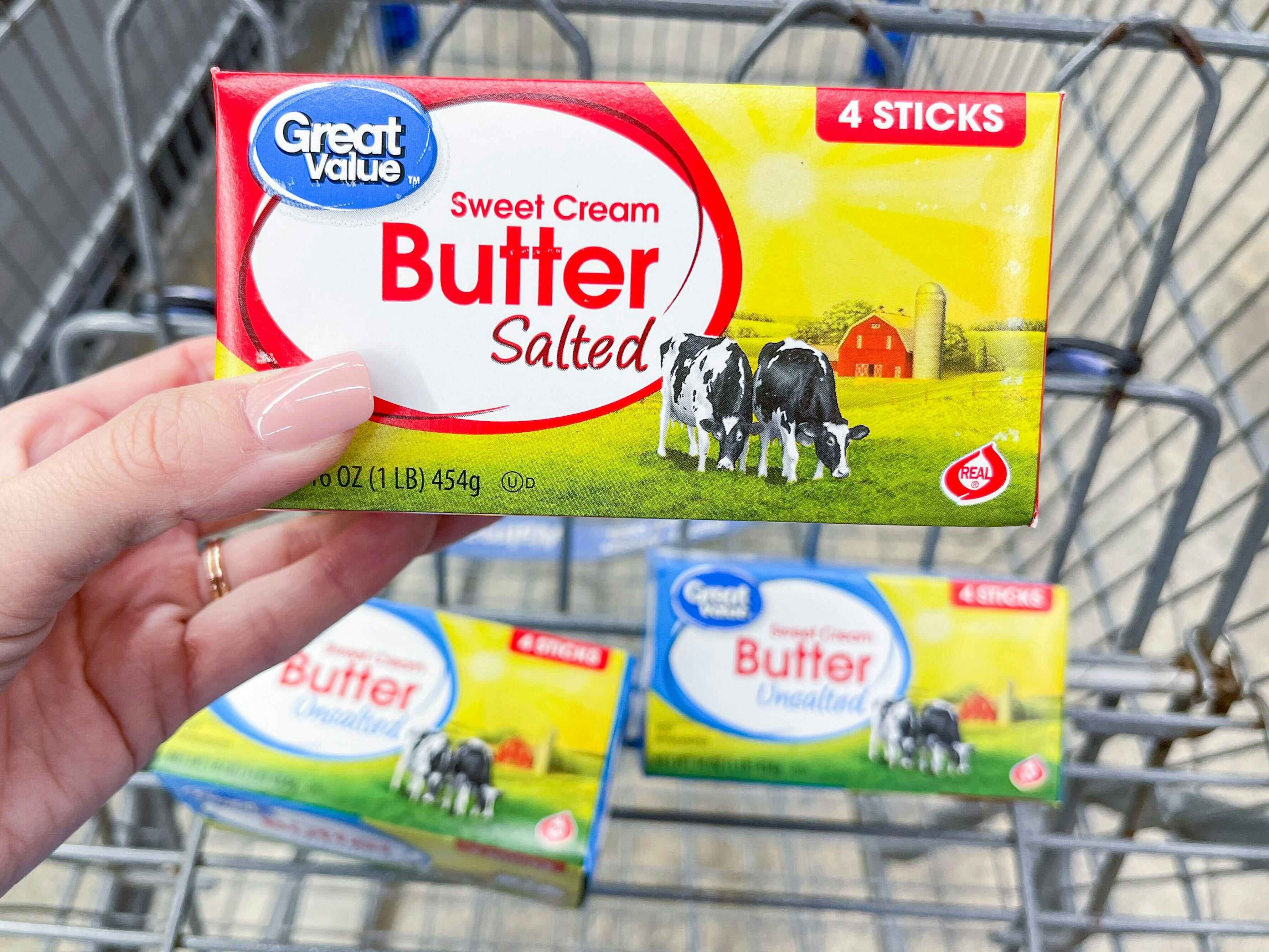 Someone holding some Great Value butter in front of more butter in a Walmart shopping cart