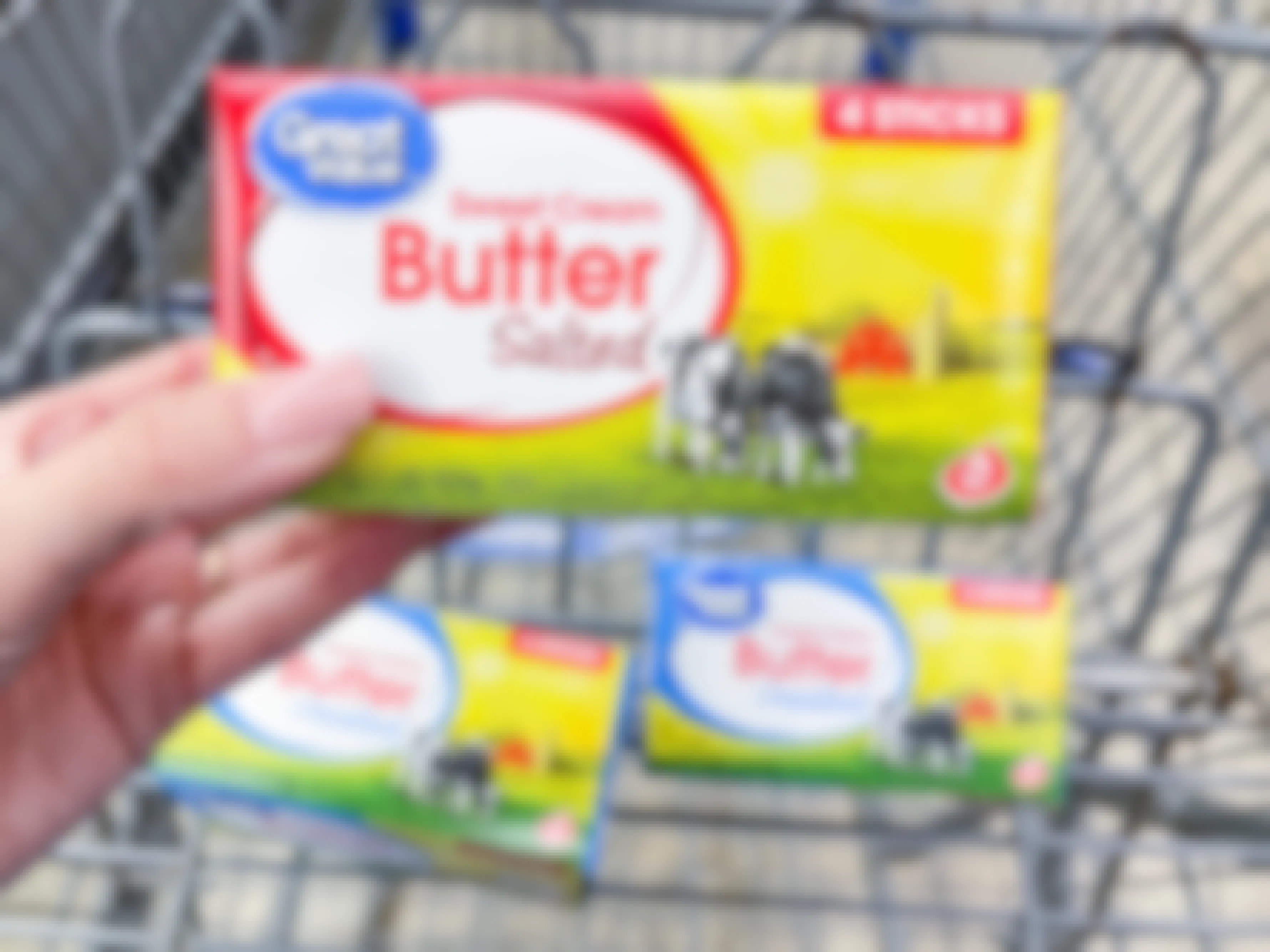 Someone holding some Great Value butter in front of more butter in a Walmart shopping cart