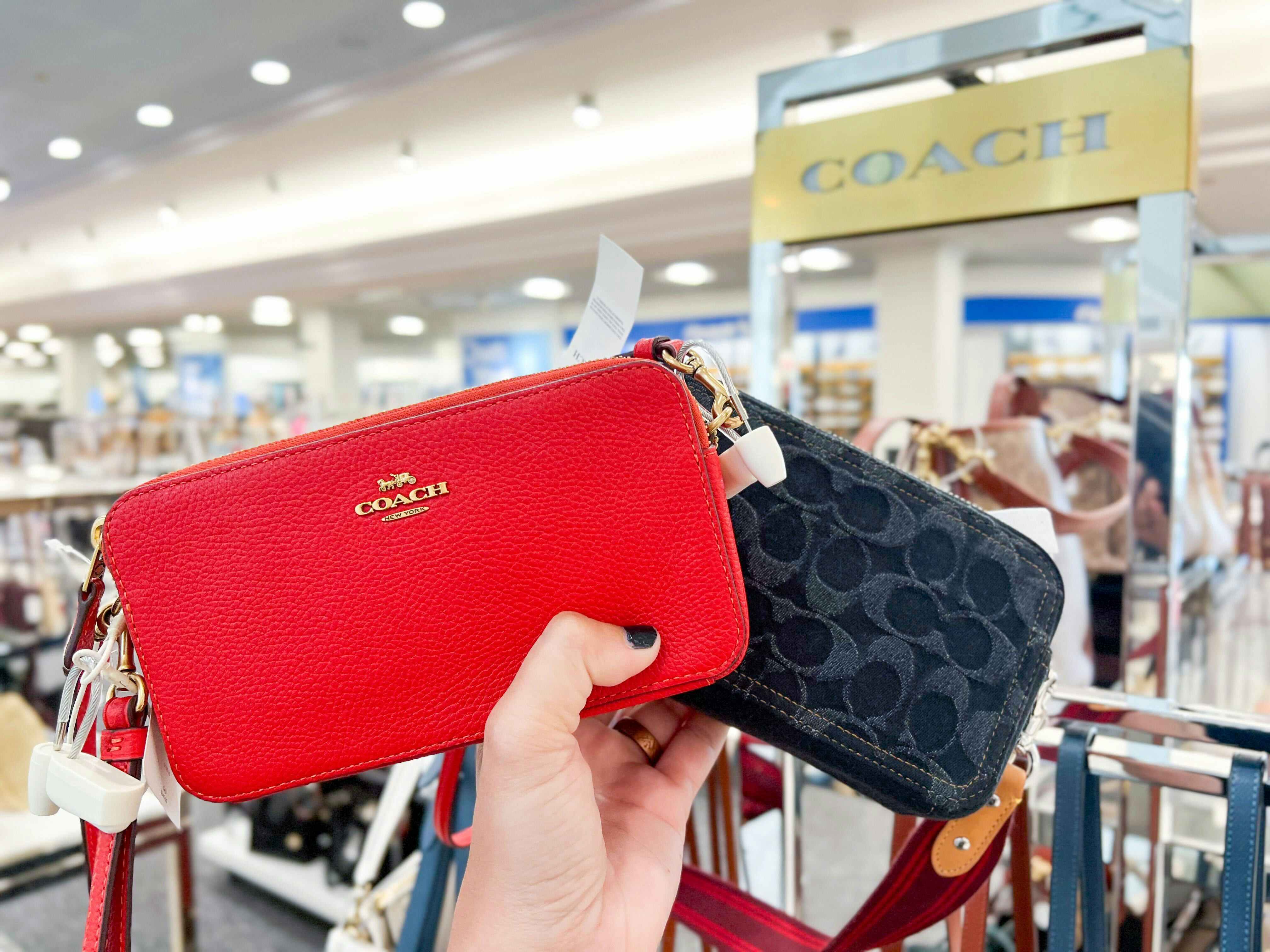 two coach wallets being held up in a coach outlet store 
