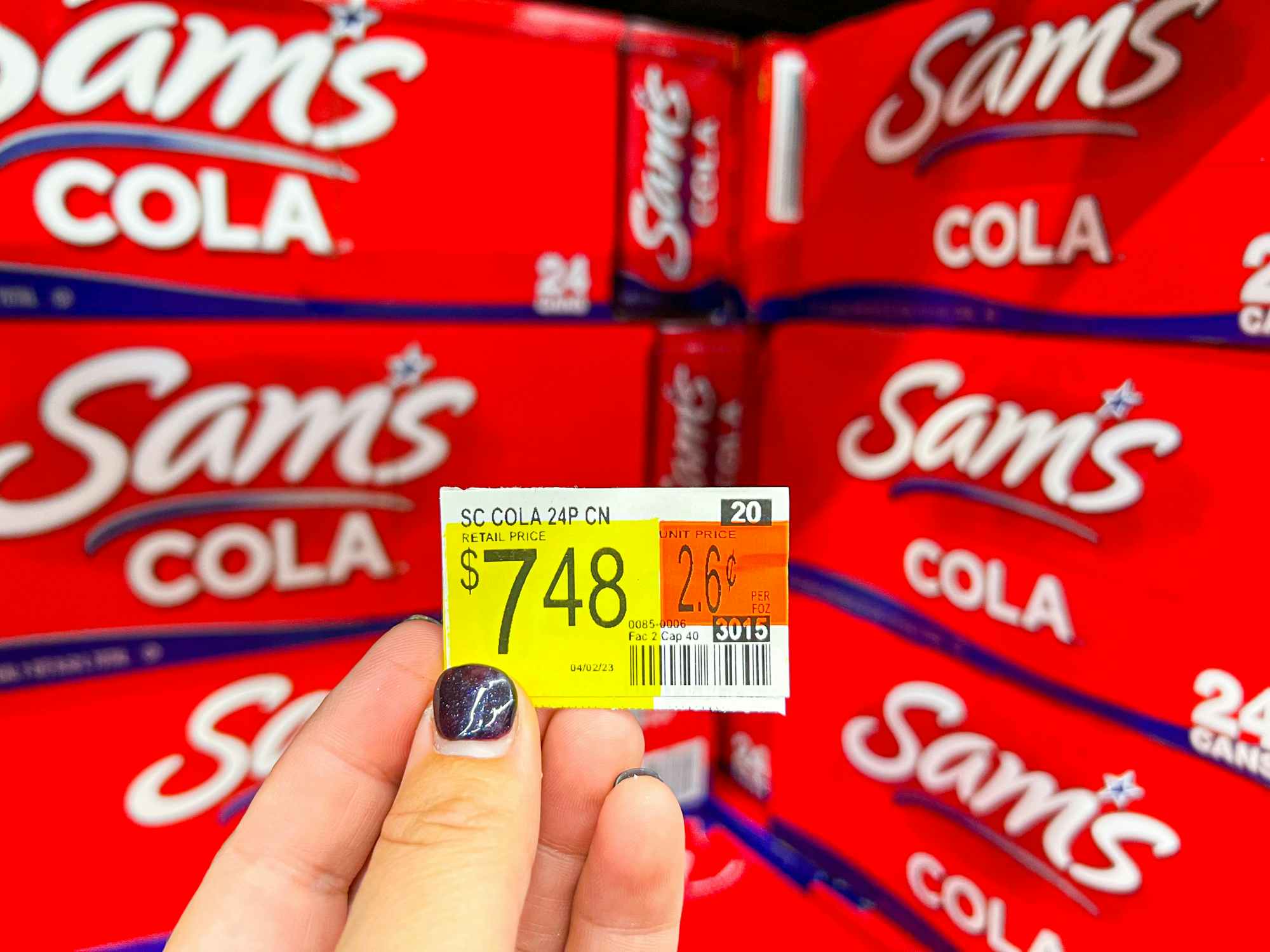 Someone holding a price tag reading $7.48 in front of a shelf of Sam's Cola at Walmart