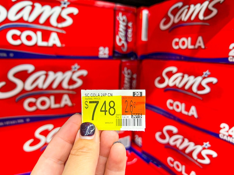 Someone holding a price tag reading $7.48 in front of a shelf of Sam's Cola at Walmart