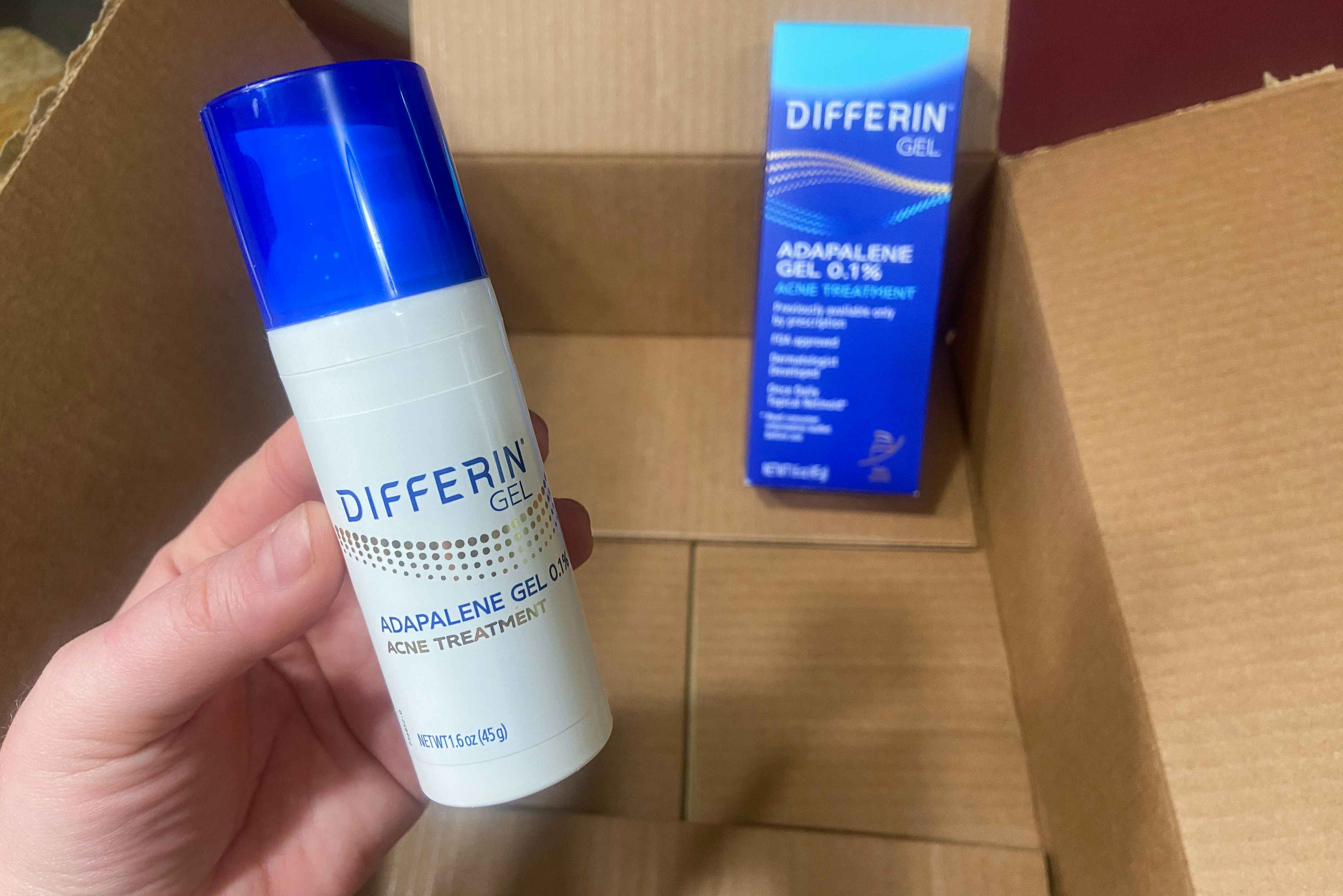 hand holding differin adapalene retinoid acne gel over an amazon box