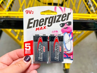 Someone holding a pack of Energizer batteries next to a Dollar General shopping cart