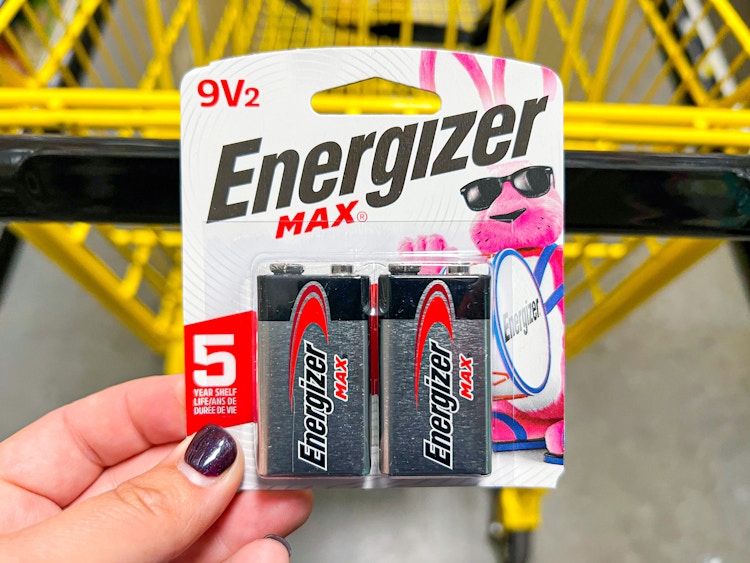 Someone holding a pack of Energizer batteries next to a Dollar General shopping cart