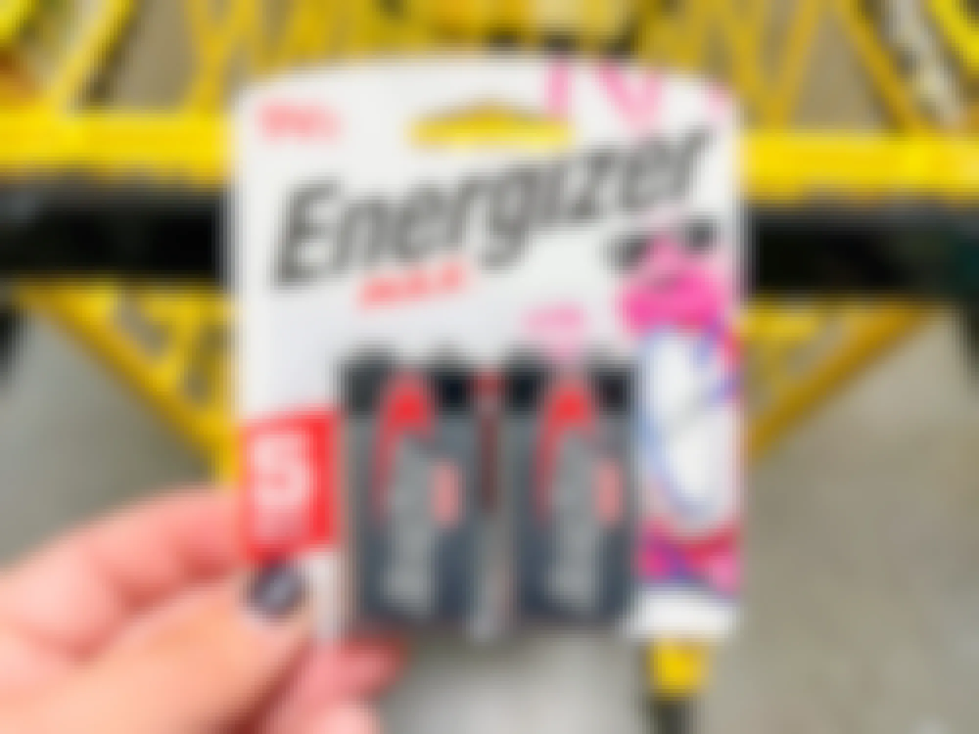 Someone holding a pack of Energizer batteries next to a Dollar General shopping cart