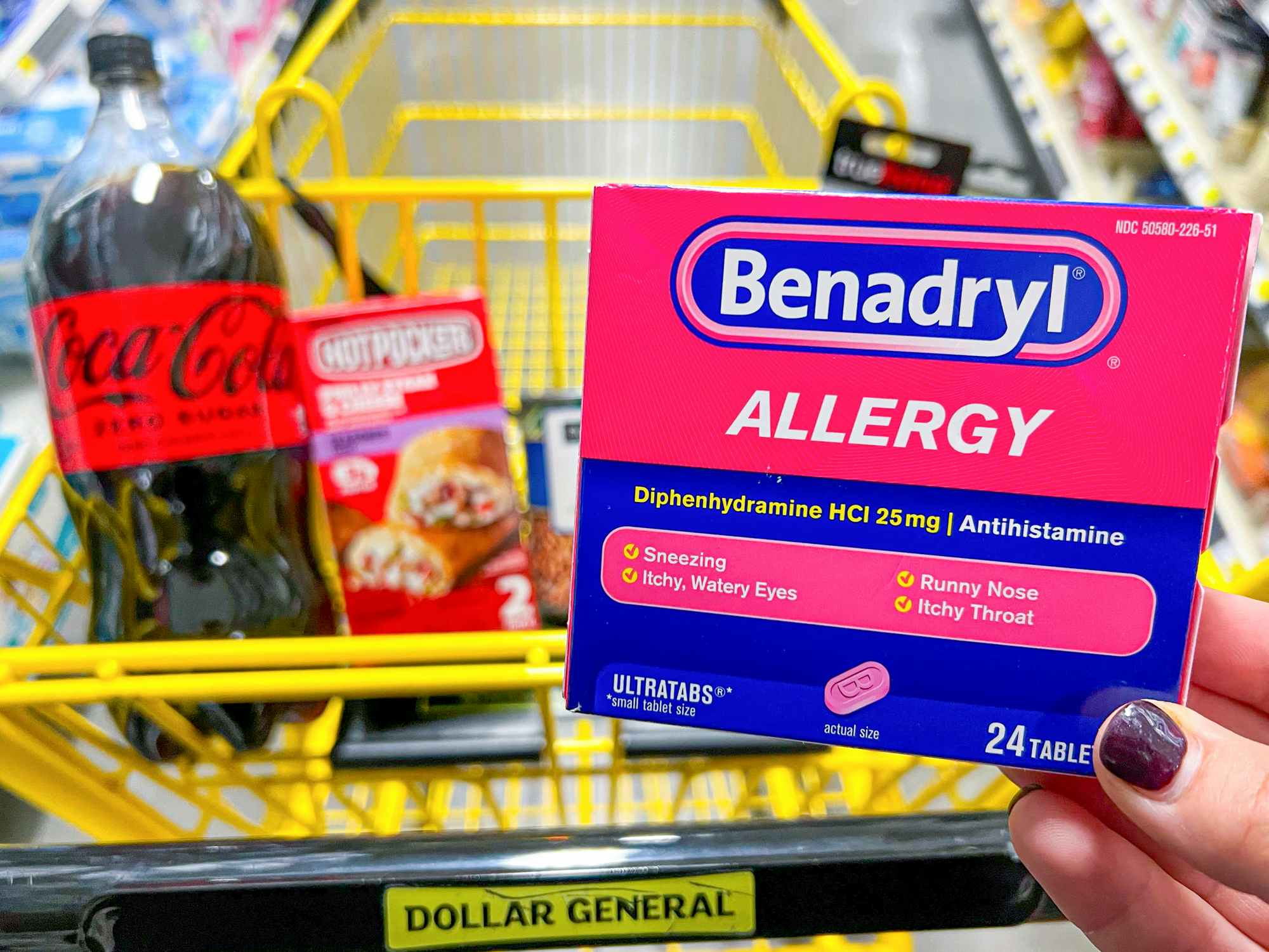 Someone holding up a box of Benadryl allergy medication next to a cart at Dollar General