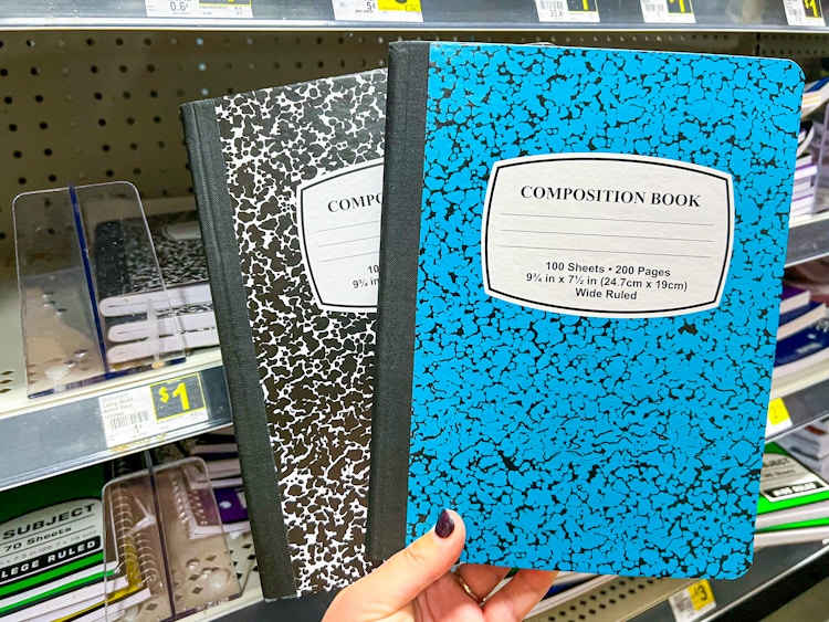 Someone holding up two composition notebooks next to a shelf at Dollar General