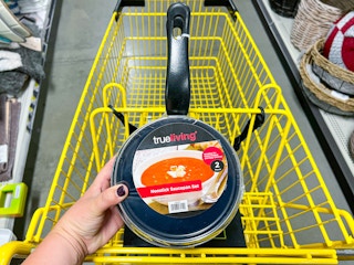 Someone holding a 2pk of Trueliving sauce pans over a Dollar General shopping cart