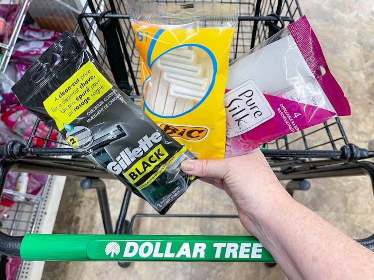 a person holding razor packages in front of dollar tree cart
