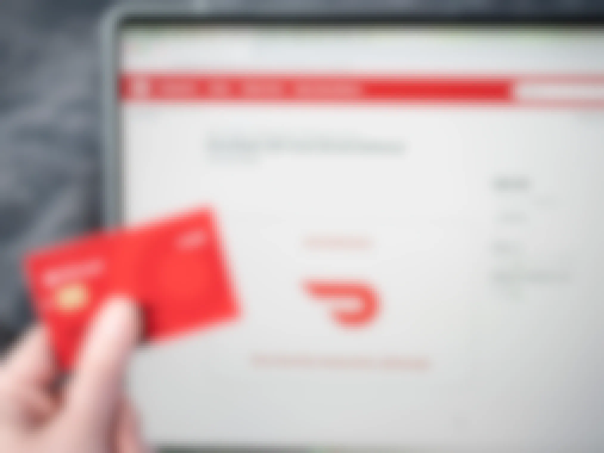 A hand holding a target red card in front of a computer screen showing DoorDash email gift cards on Target.com