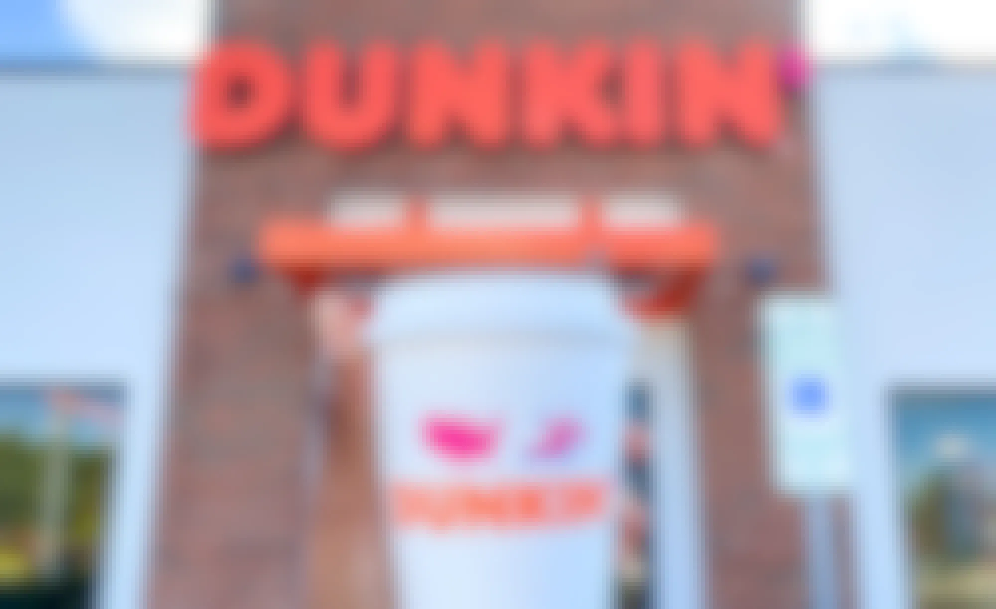 person holding a hot cup of dunkin donuts coffee in front of restaurant entrance