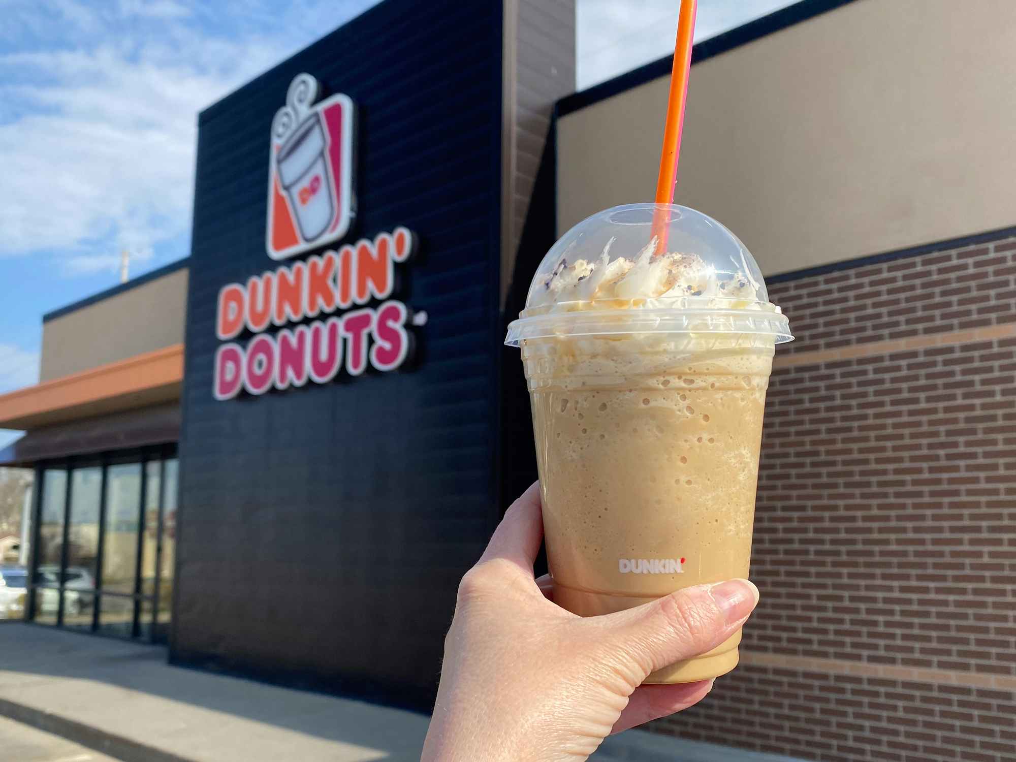 person holding dunkin donuts frozen butter pecan swirl drink outside restaurant