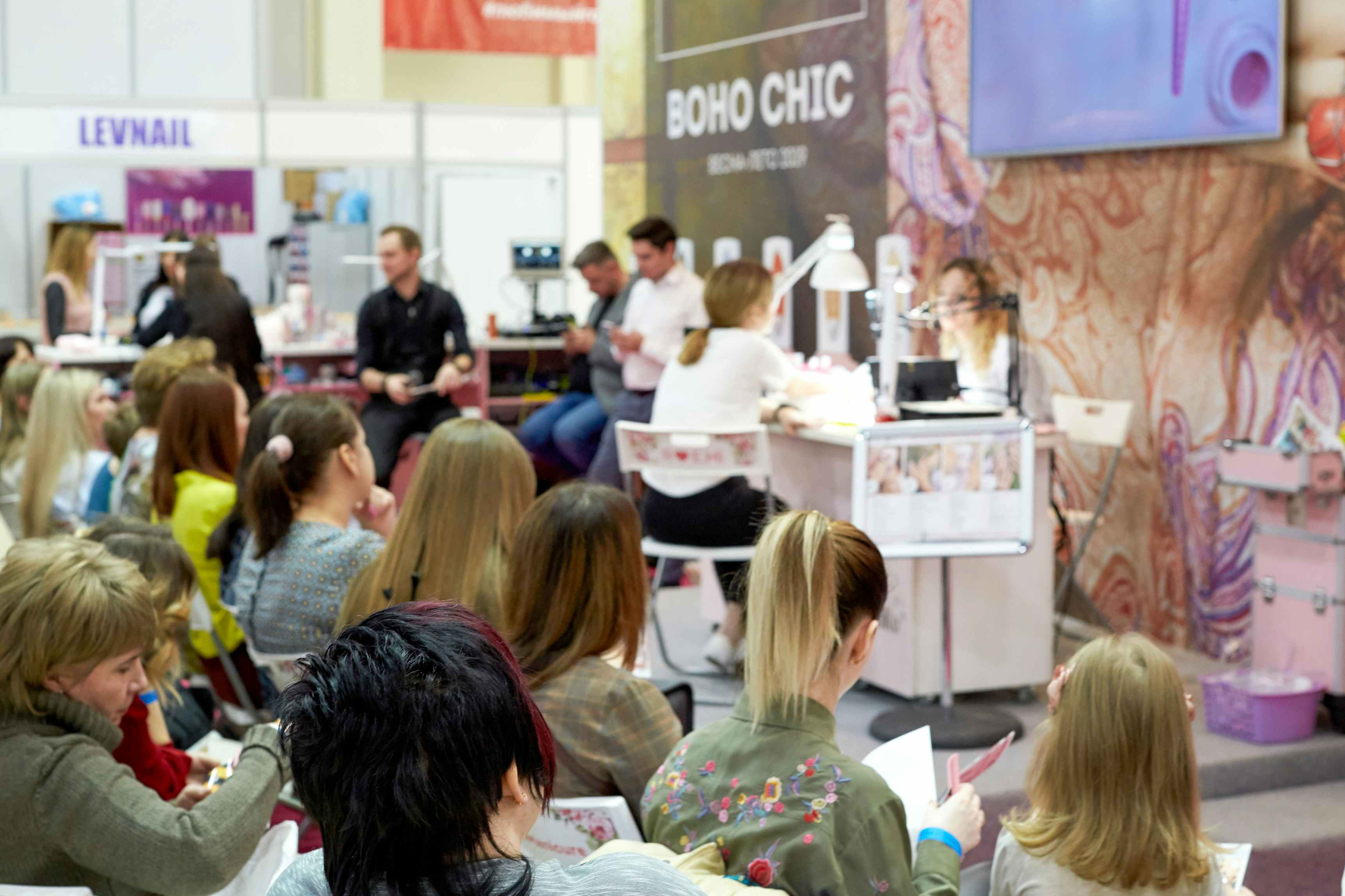 People at a Beauty Expo watching someone do a manicure at a booth