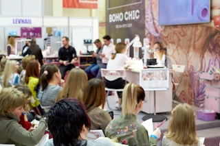 People at a Beauty Expo watching someone do a manicure at a booth