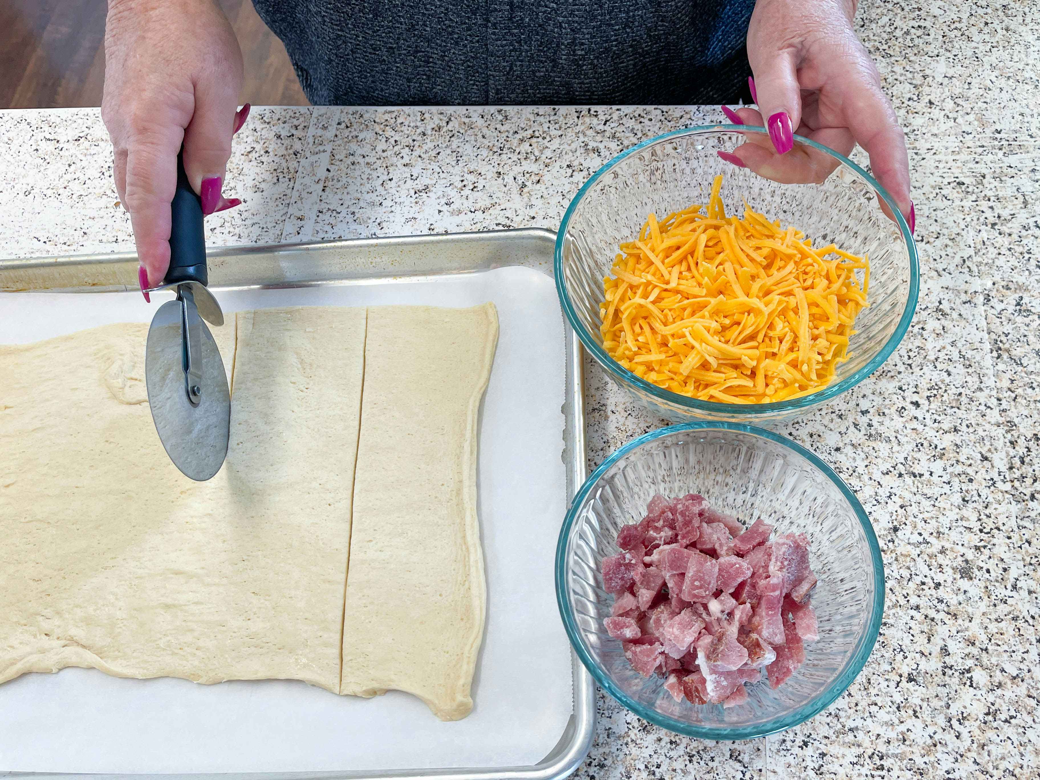 a person cutting dough with cheese and ham 