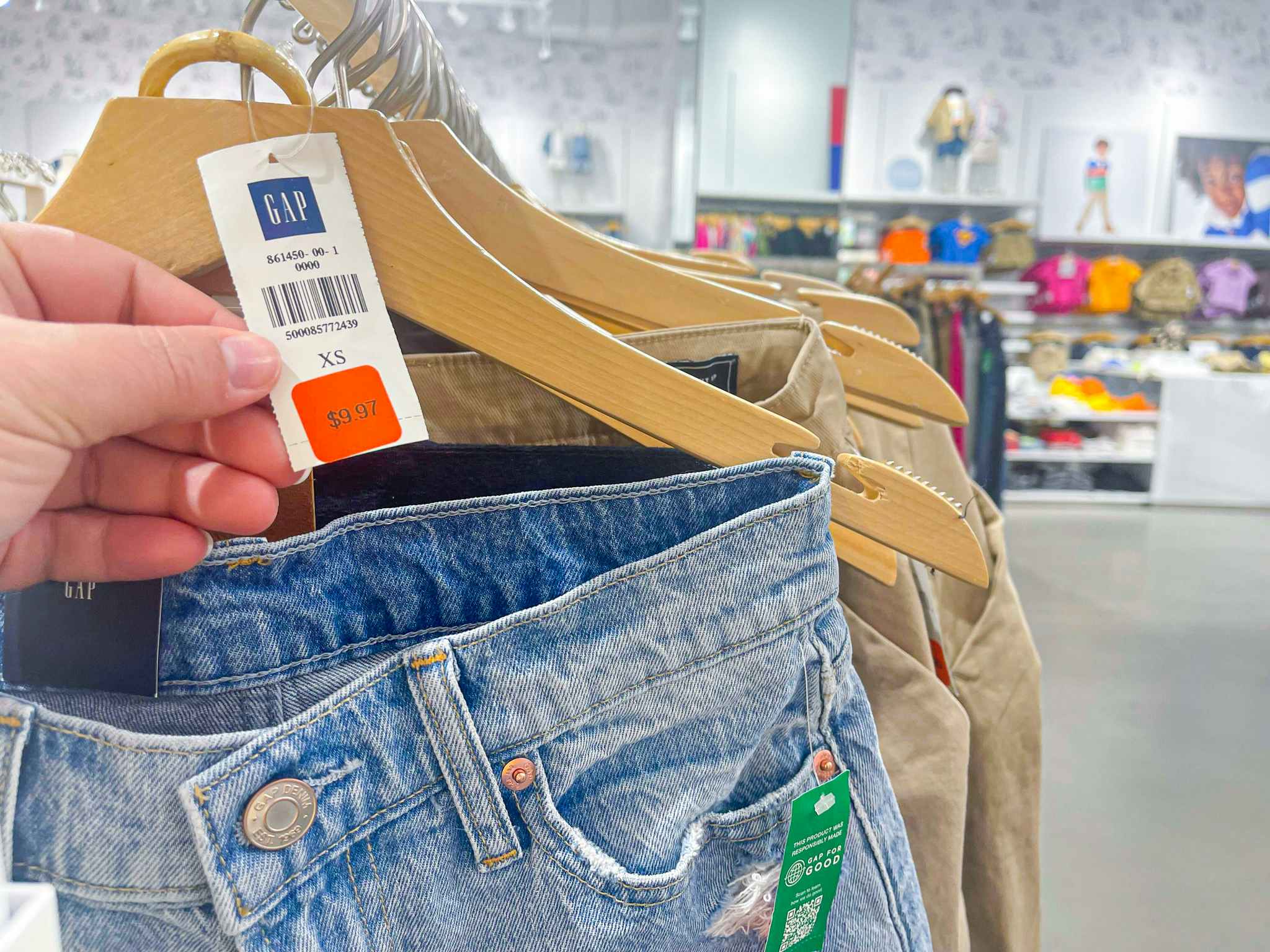 a person holding a gap orange tag on a pair of jeans on rack in store 