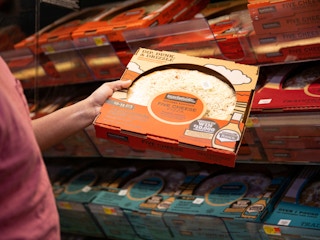 Person grabbing a five cheese walmart pizza from a cooler