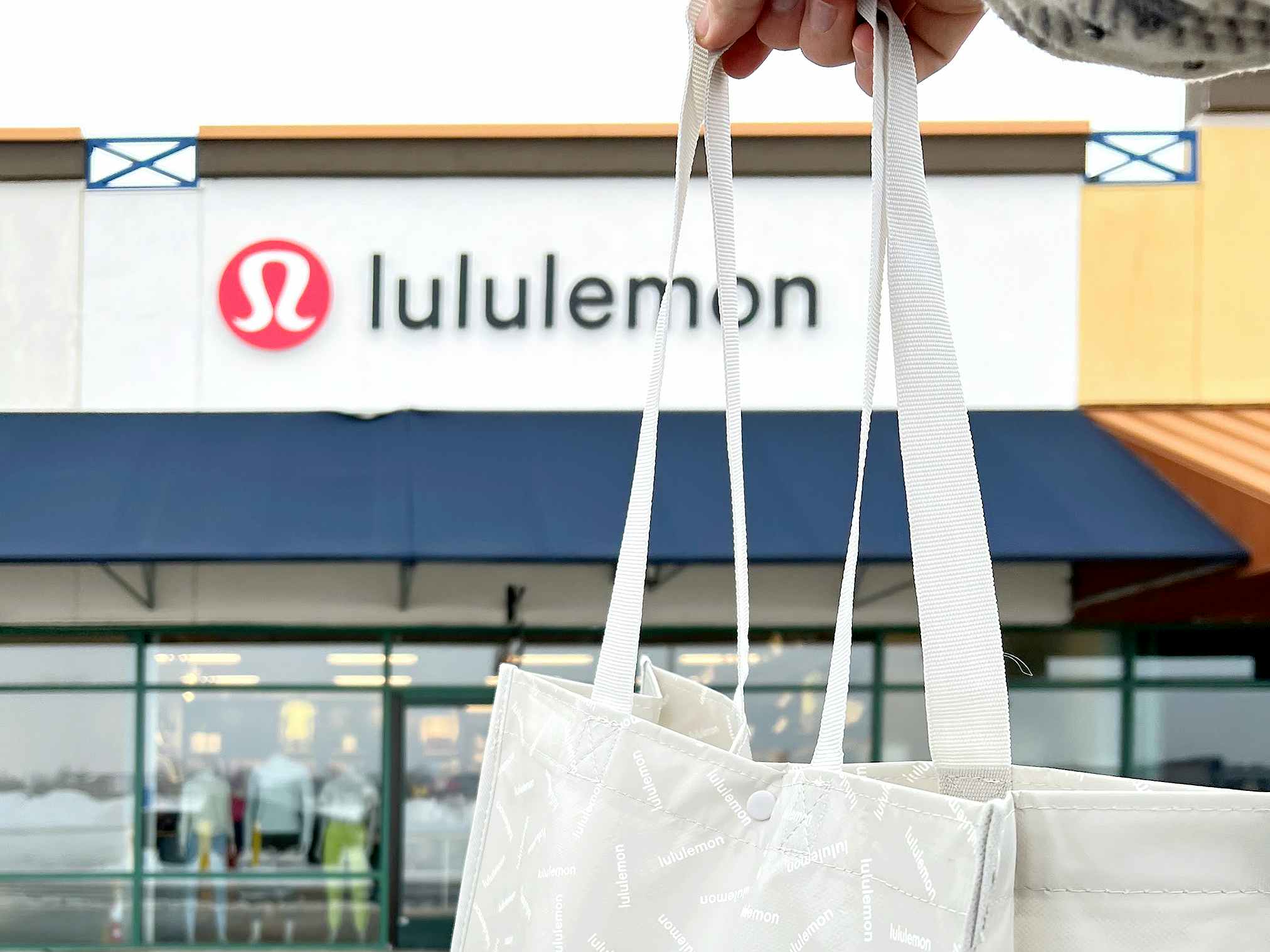 person holding reusable bag in front of lululemon outlet store entrance