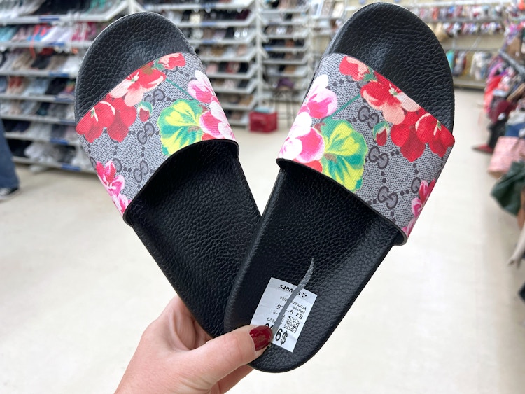 person holding a pair of floral gucci slides at a thrift store