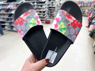 person holding a pair of floral gucci slides at a thrift store