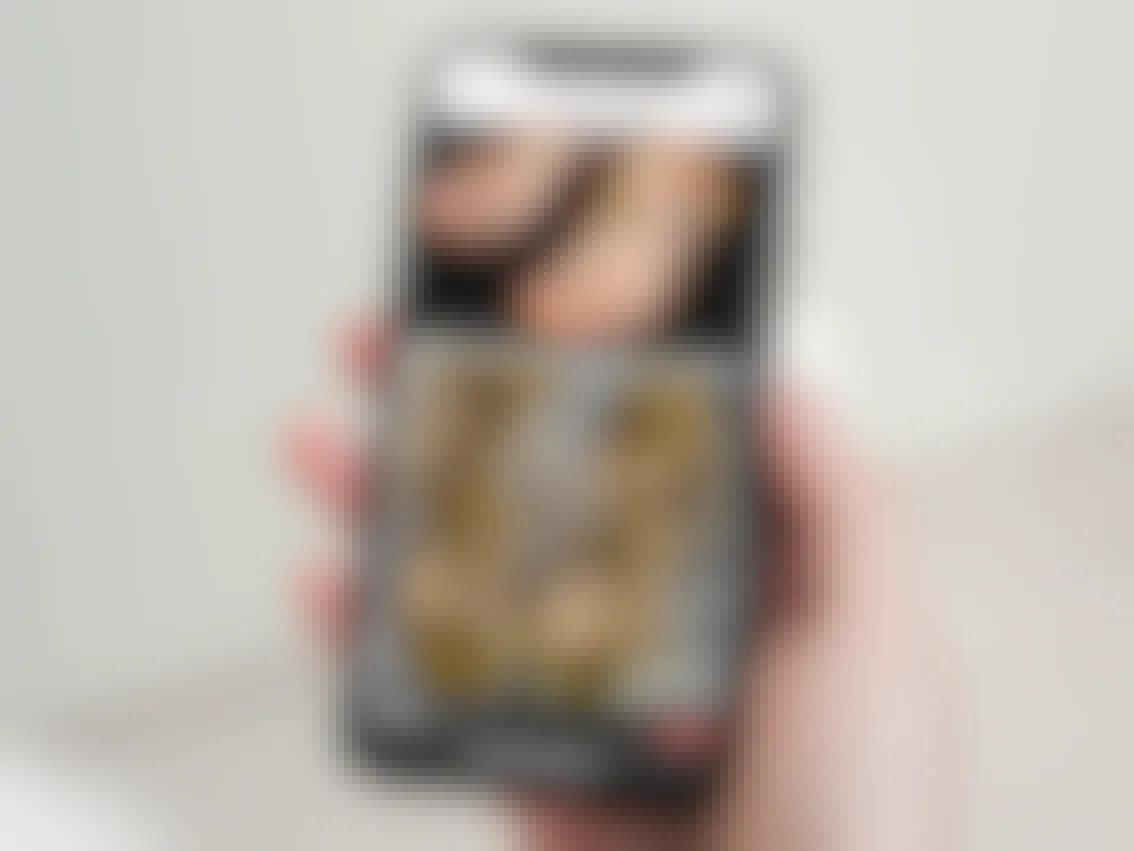 person holding a phone with a screenshot of a pair of designer gold sandals that sold