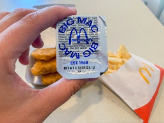 a person holding a big mac sauce cup in front of nuggets and fries at McDonald's