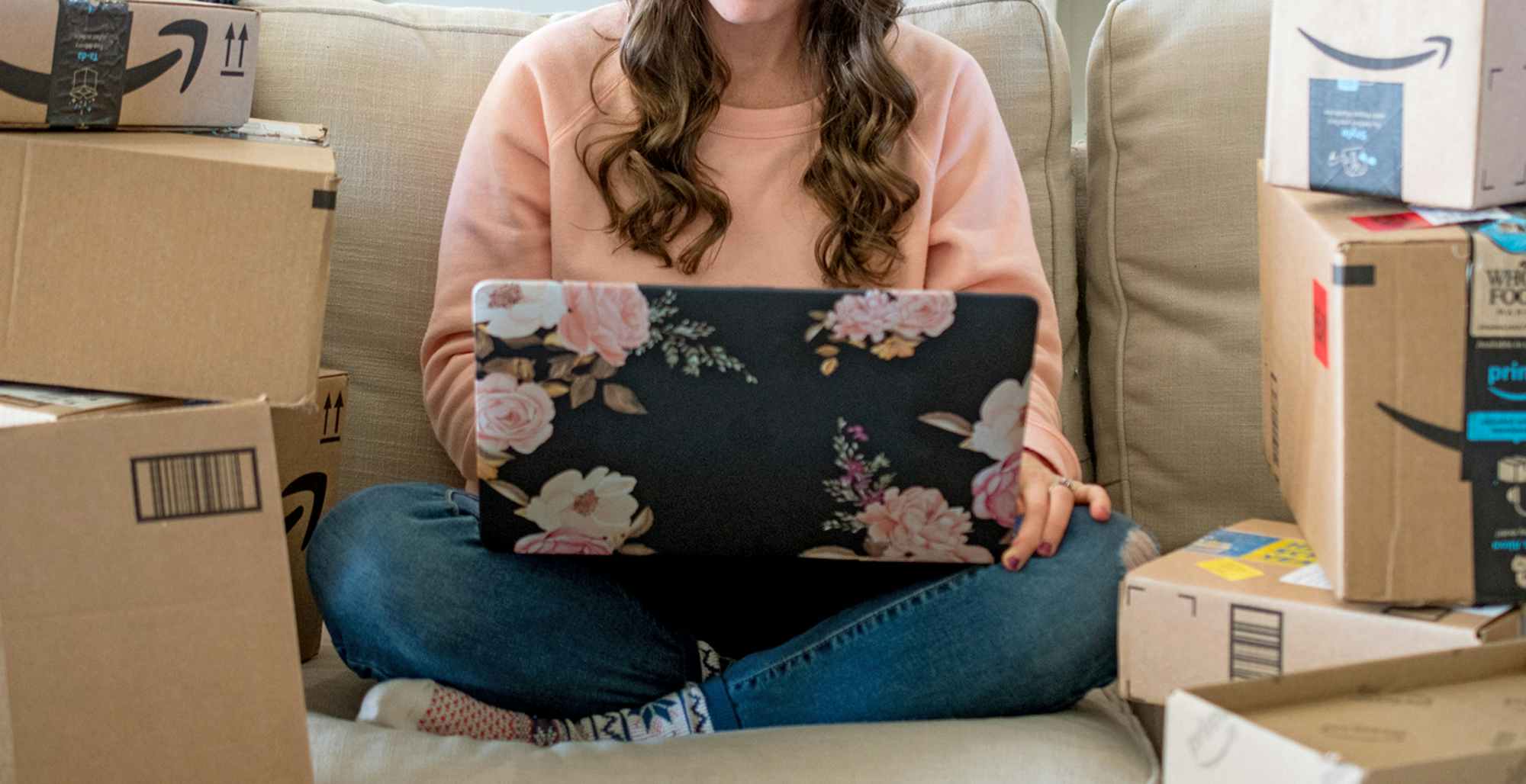 person with laptop on couch surrounded by amazon boxes