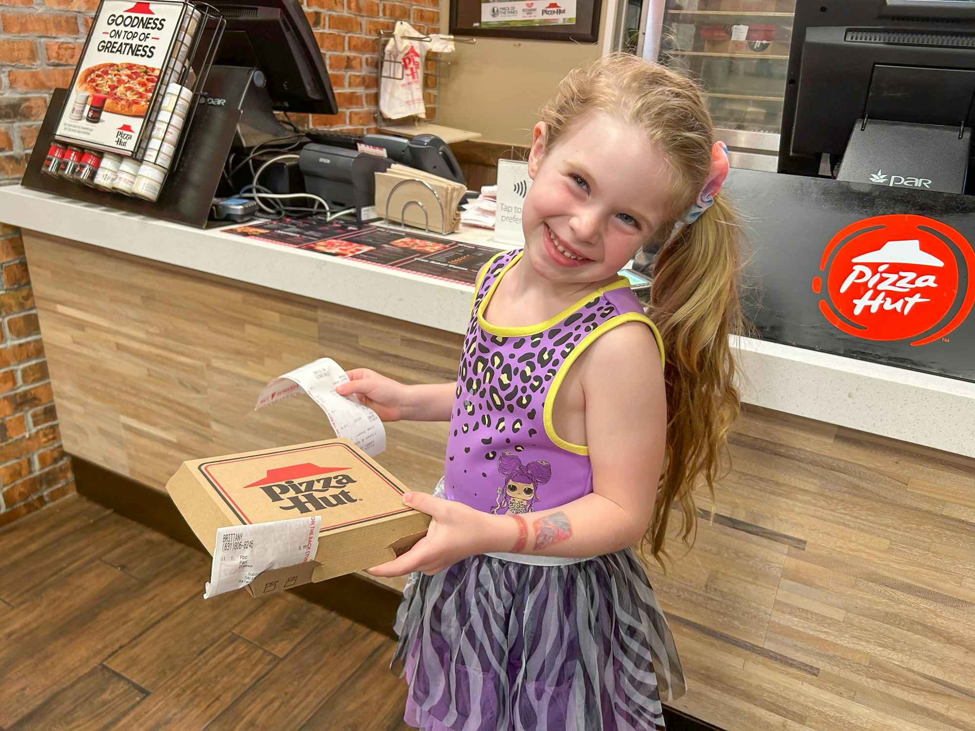 A little girl holding a personal pizza from Pizza Hut with a receipt showing it being free with the Book It promotion