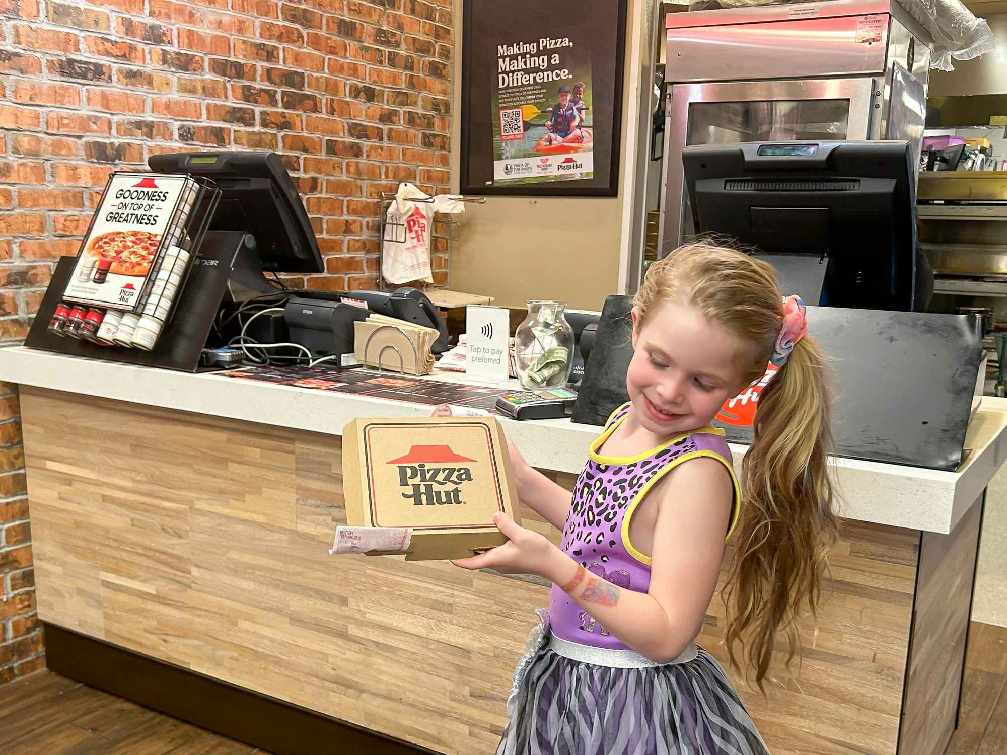 A little girl holding a personal pizza from Pizza Hut with a receipt showing it being free with the Book It promotion