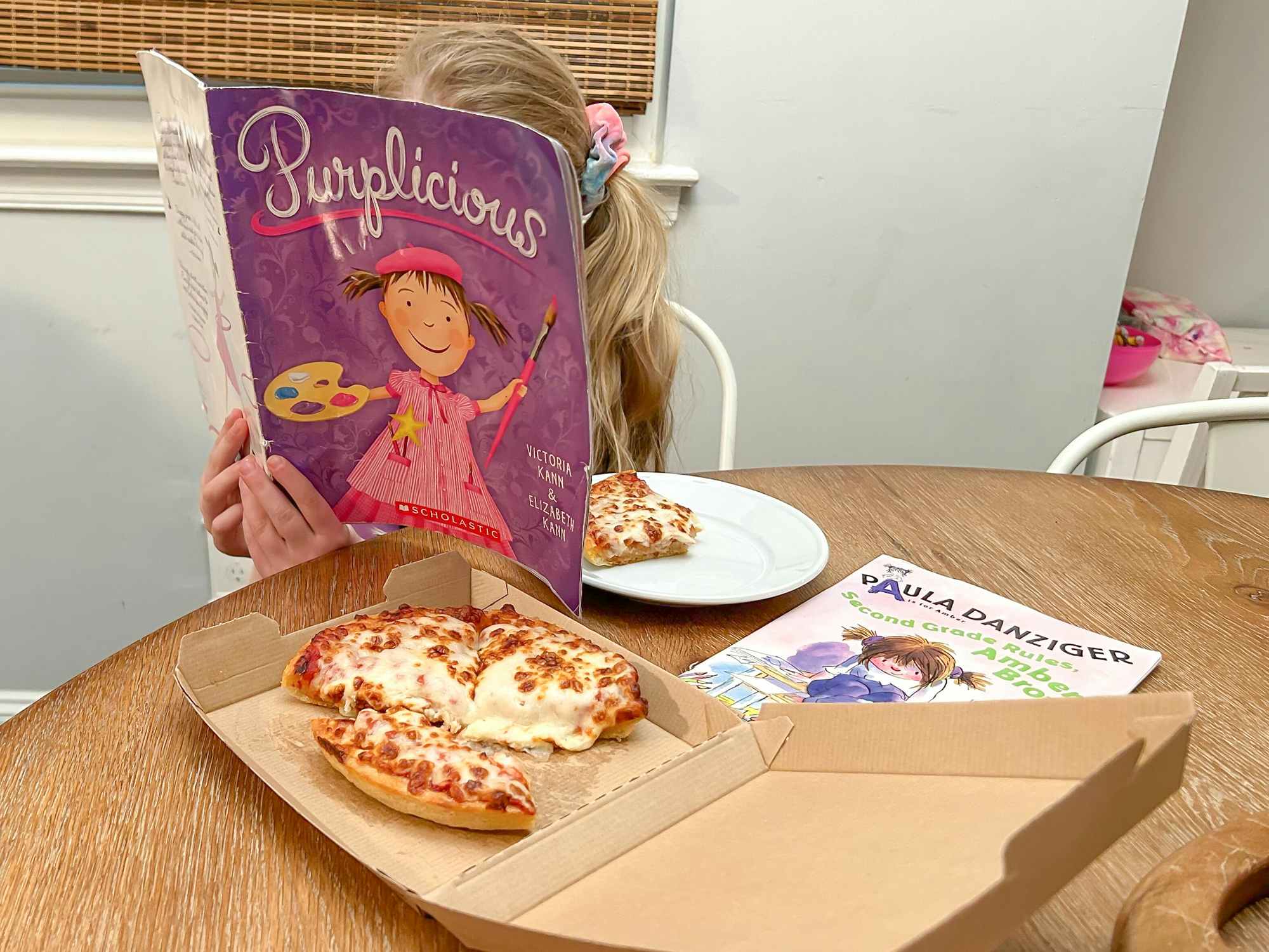 A little girl with books and a personal pizza from Pizza Hut