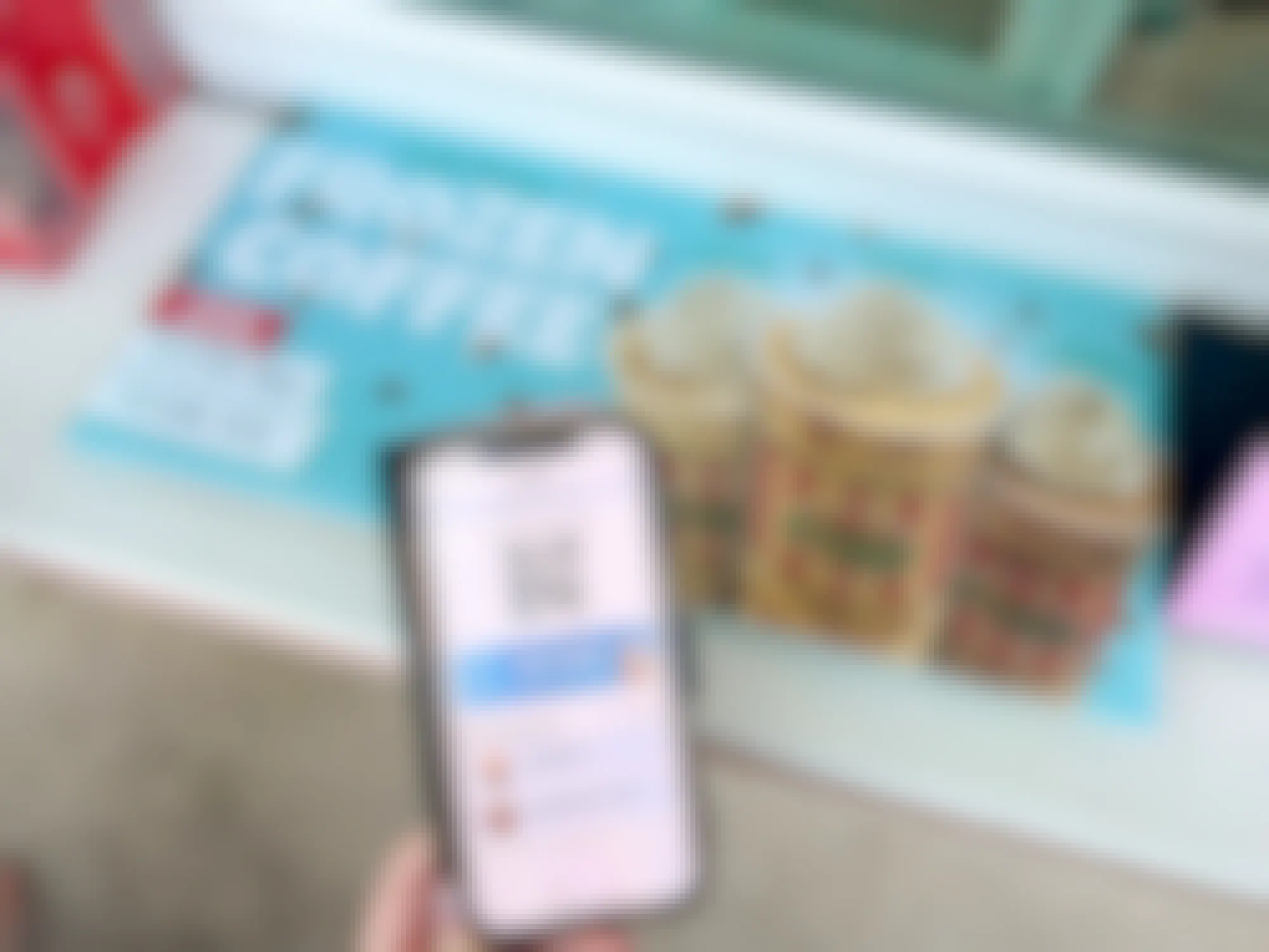 Someone holding their Rita's app next to a sign for a free small frozen coffee at Rita's