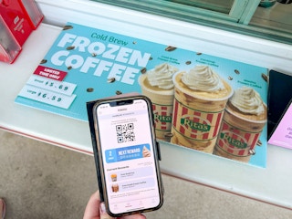 Someone holding their Rita's app next to a sign for a free small frozen coffee at Rita's
