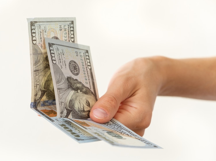 a persons hand holding two hundred dollar bills