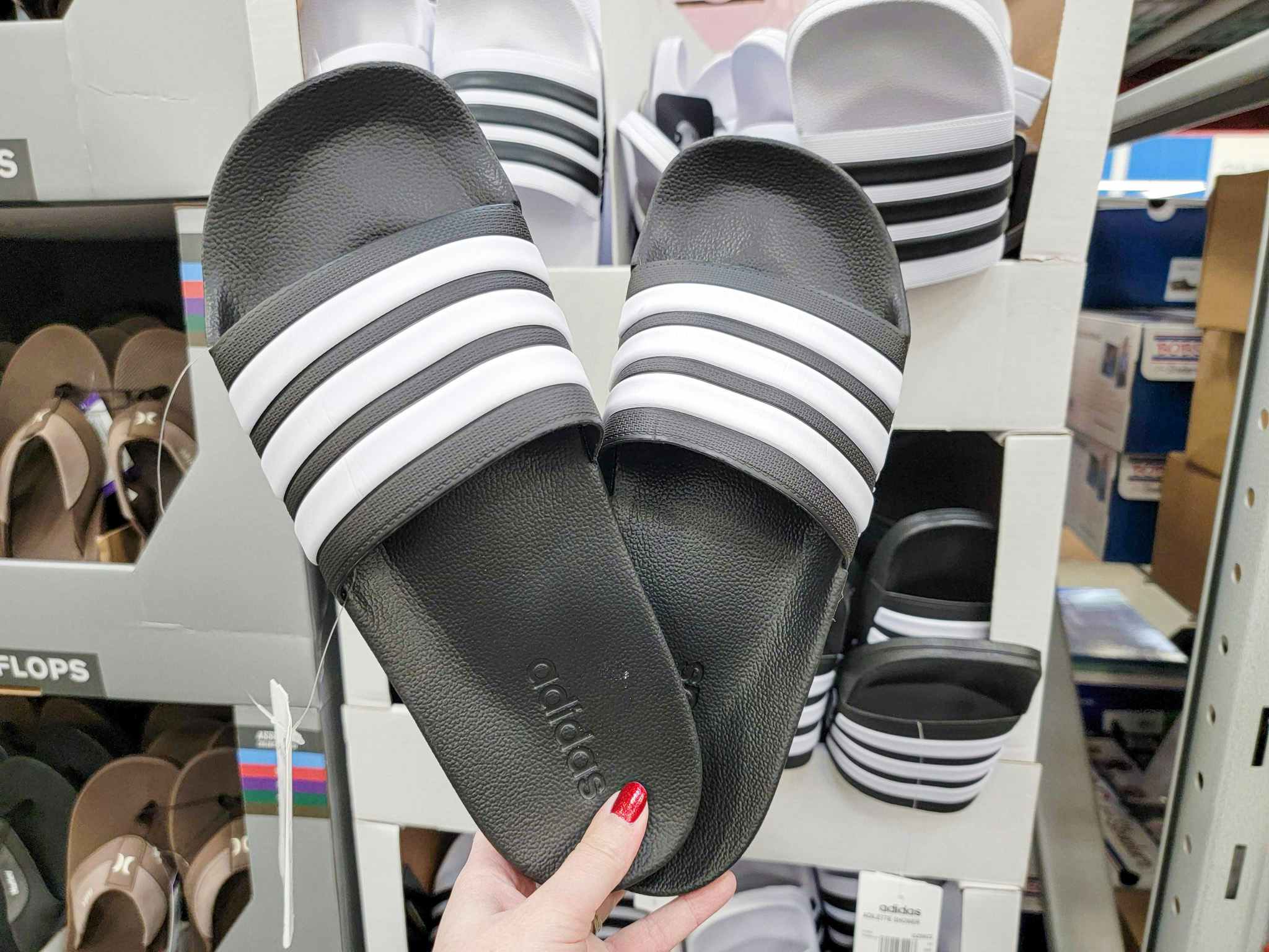 hand holding a pair of black adidas slides