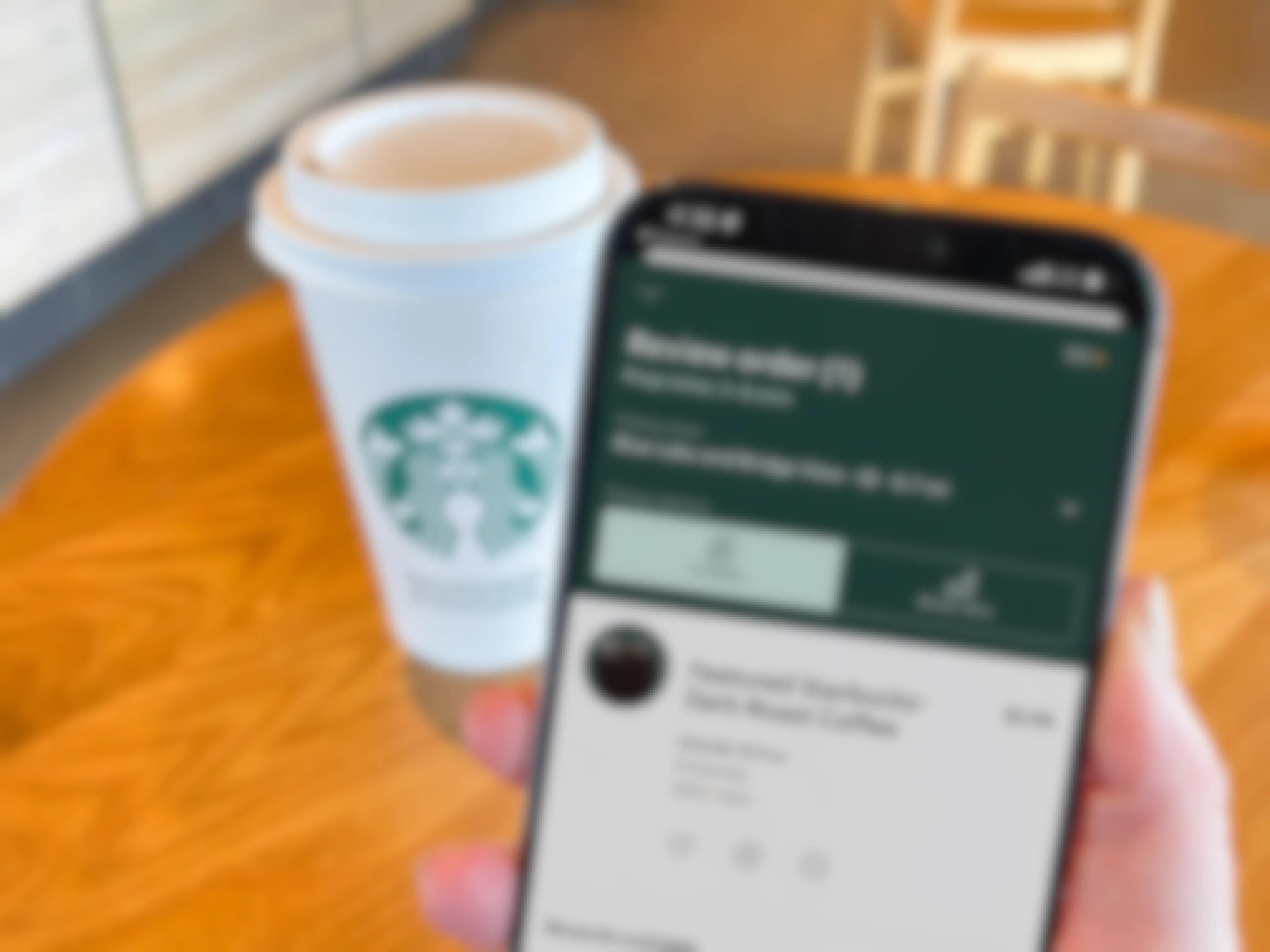 a person holding a cellphone with starbucks on screen in front of starbucks coffee