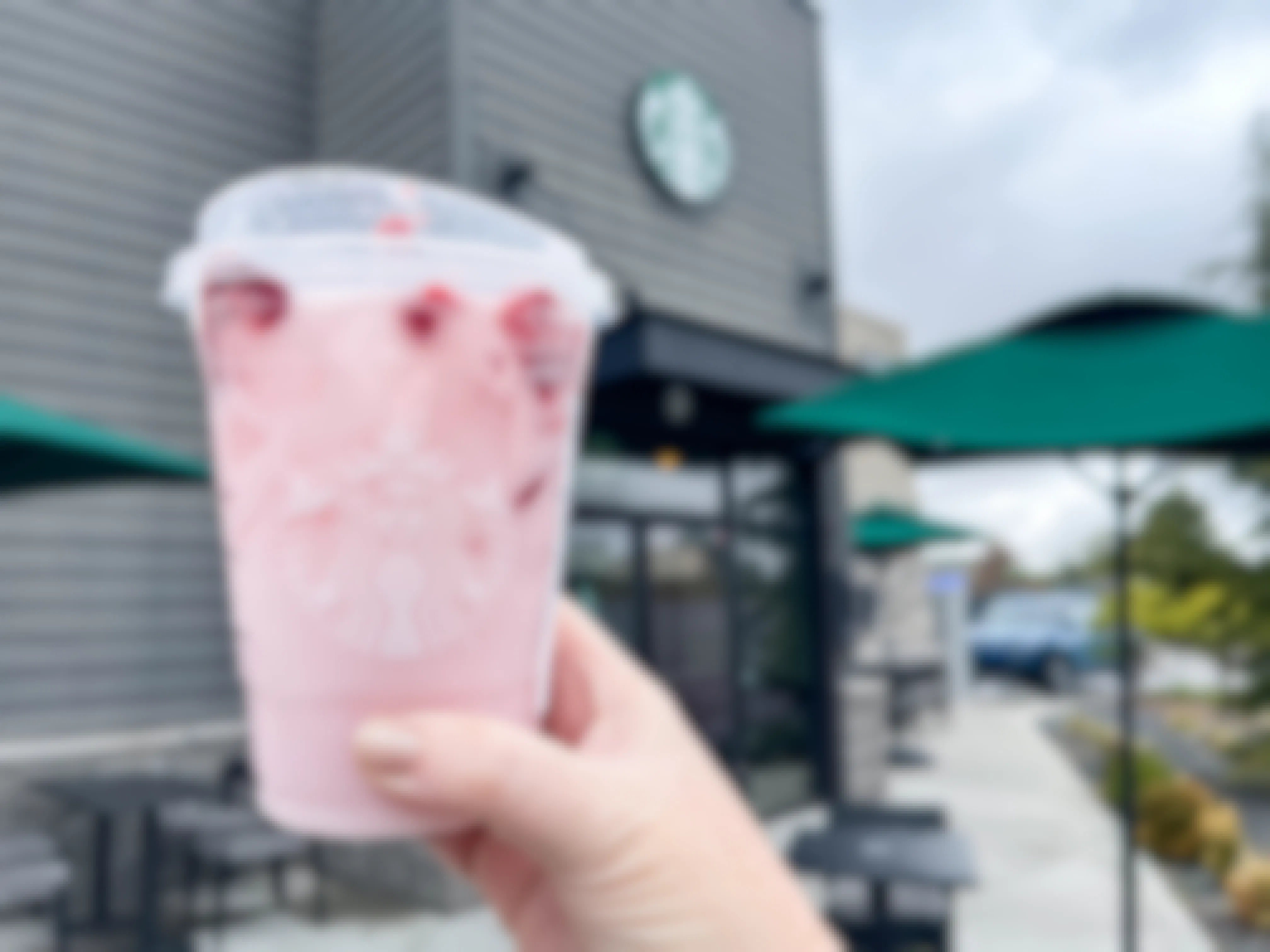 a person holding a starbucks pink drink in front of starbucks 