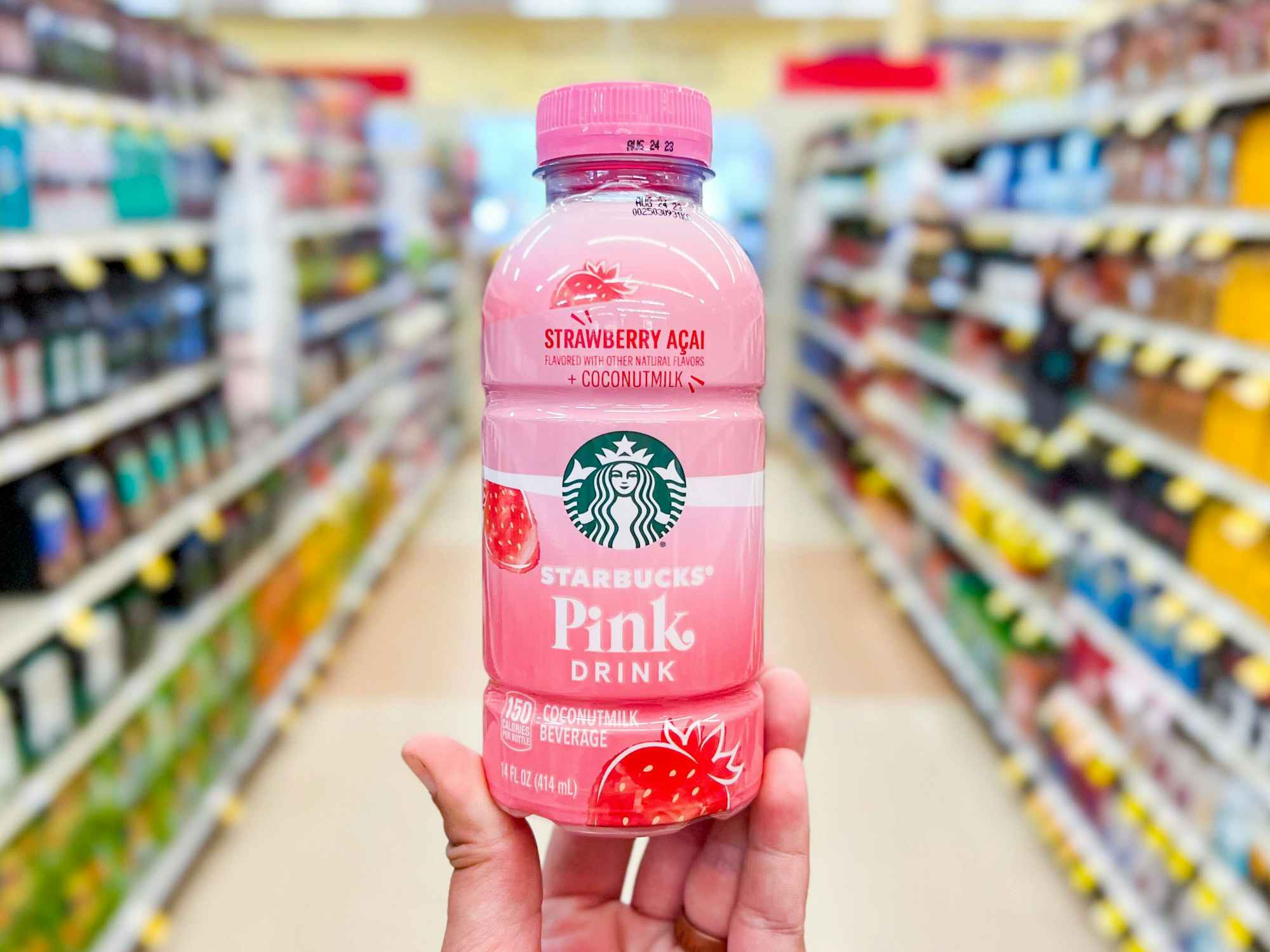 Someone holding a Starbucks bottled Pink Drink in an aisle at a grocery store