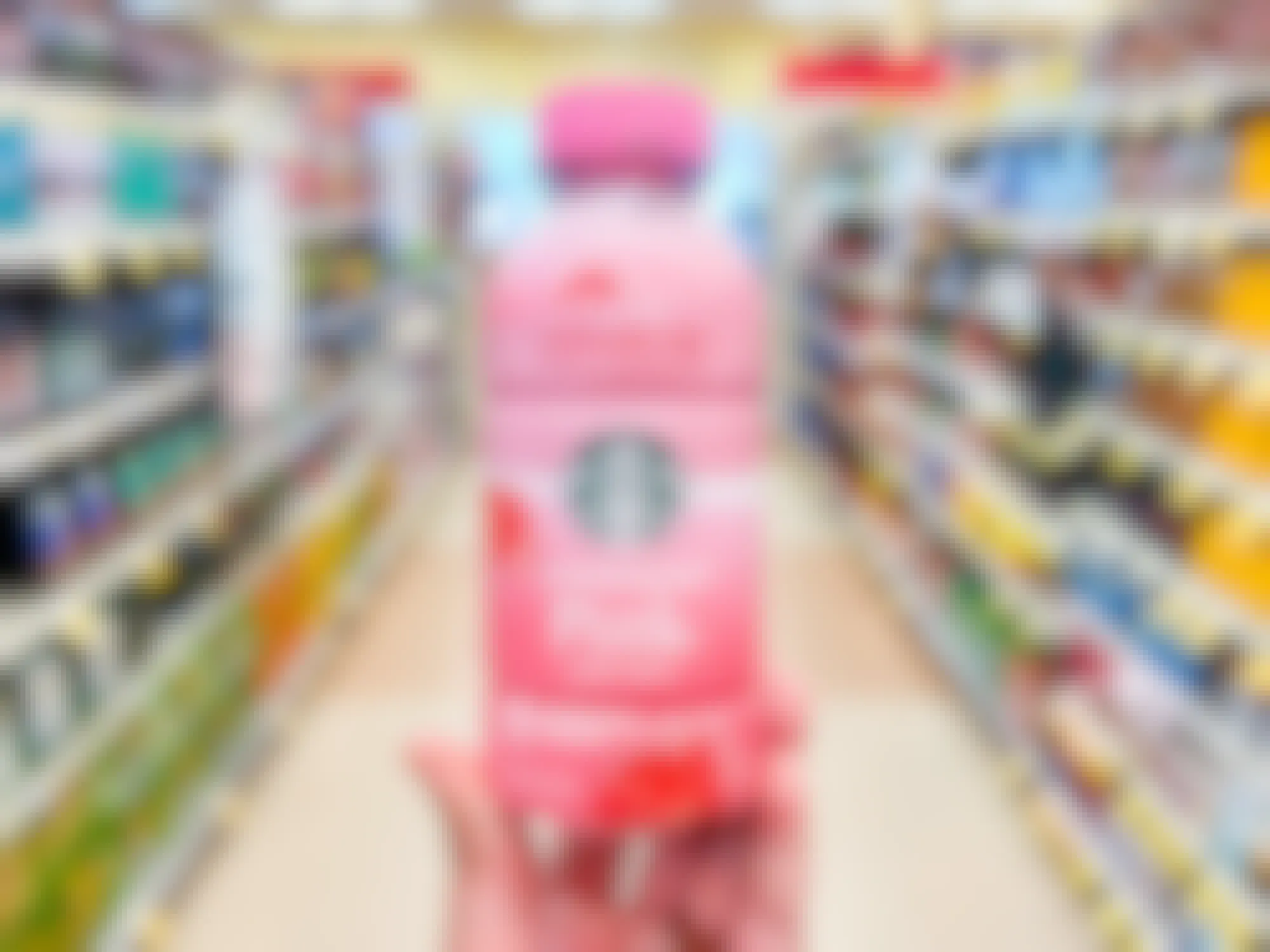 Someone holding a Starbucks bottled Pink Drink in an aisle at a grocery store